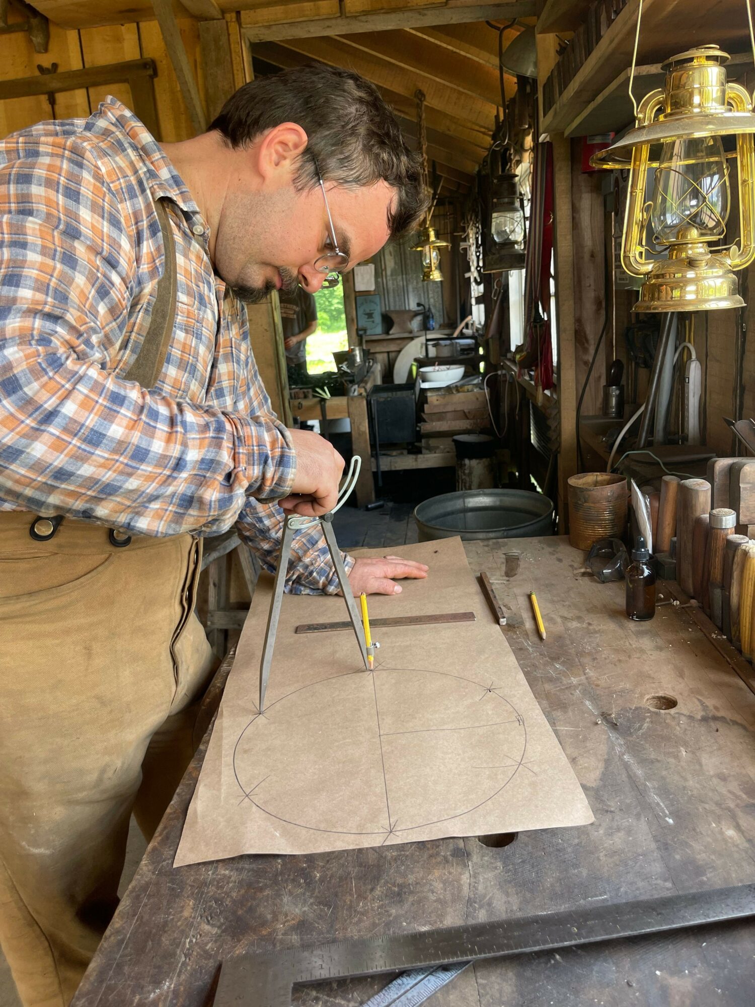 Man drawing on paper with a pencil in a workshop filled with tools and equipment.
