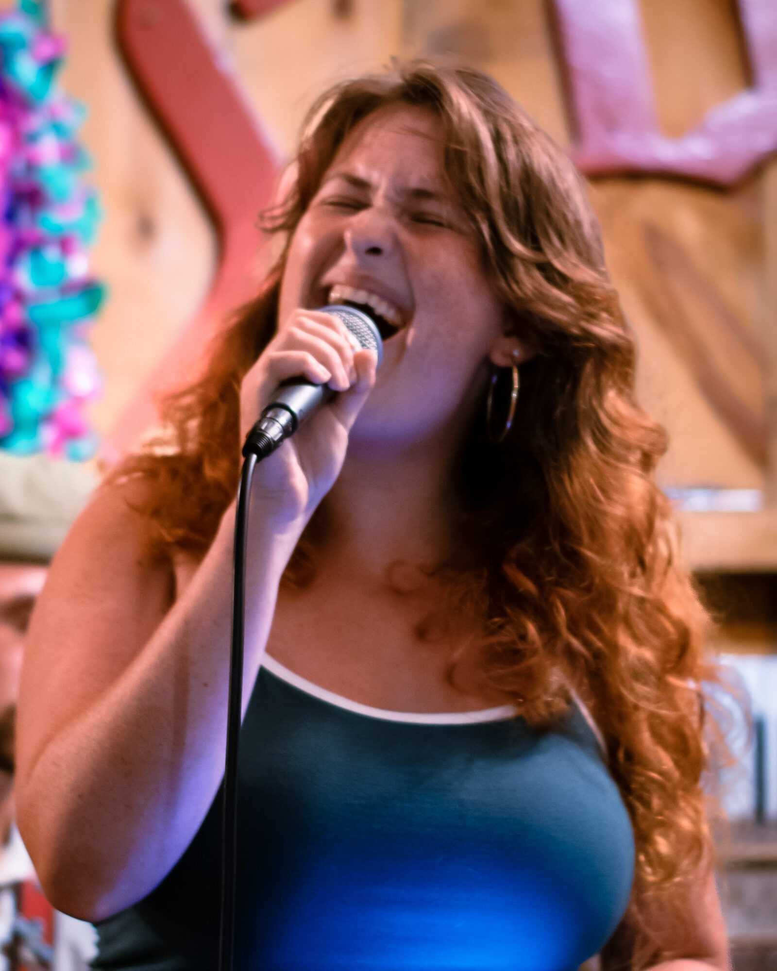 Woman singing passionately into a microphone with curly hair and a colorful background.