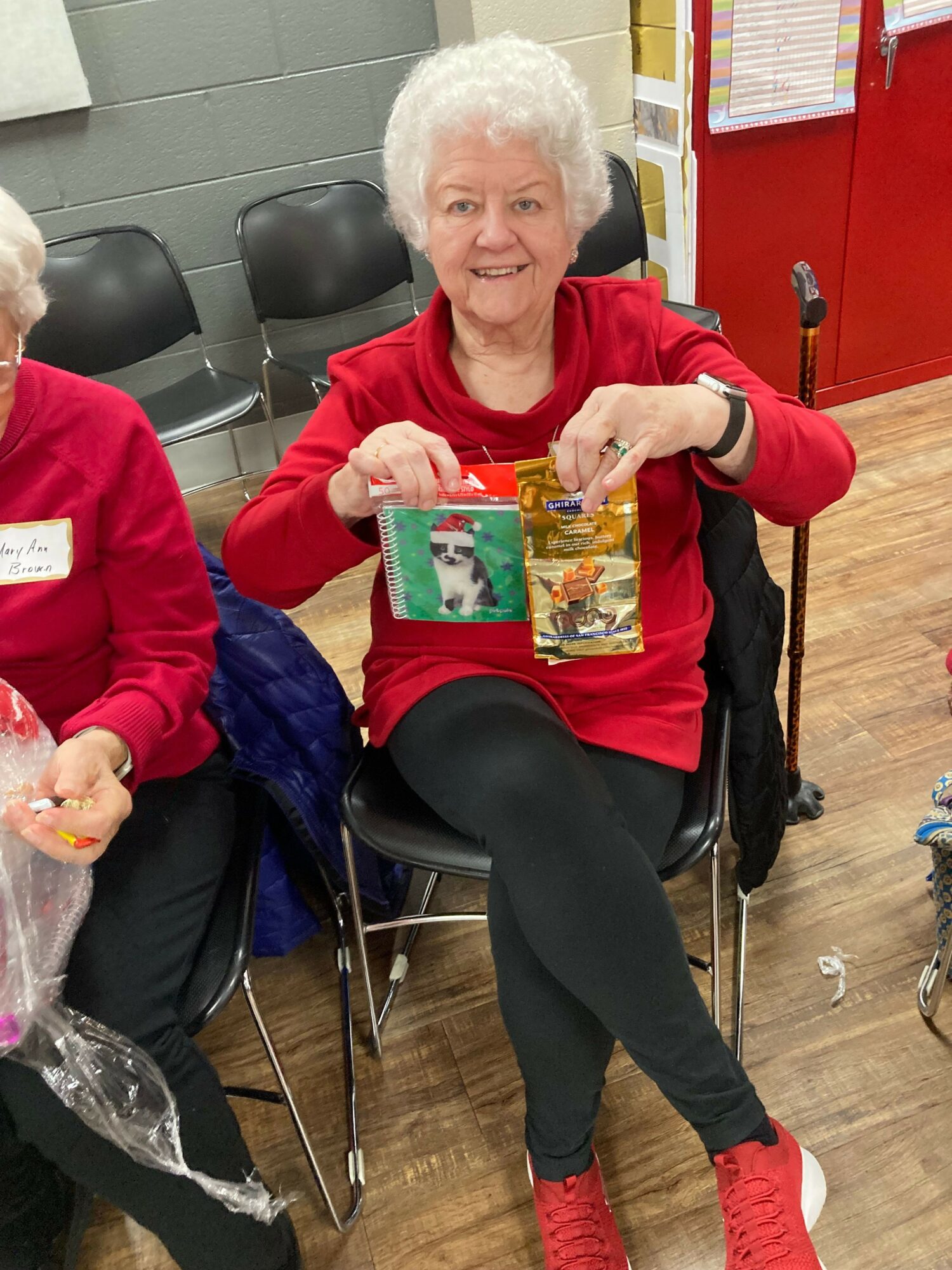 Elderly woman with white hair in red sweater sitting in a wheelchair, holding a colorful photo album, smiling.