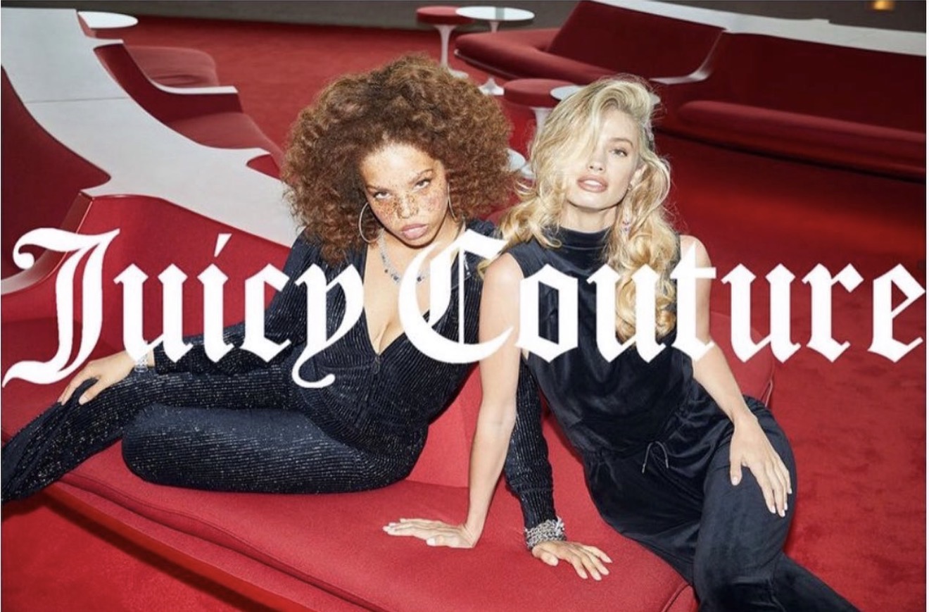 Two women with curly and straight blonde hair sitting on a red surface, with Juicy Couture logo in background.