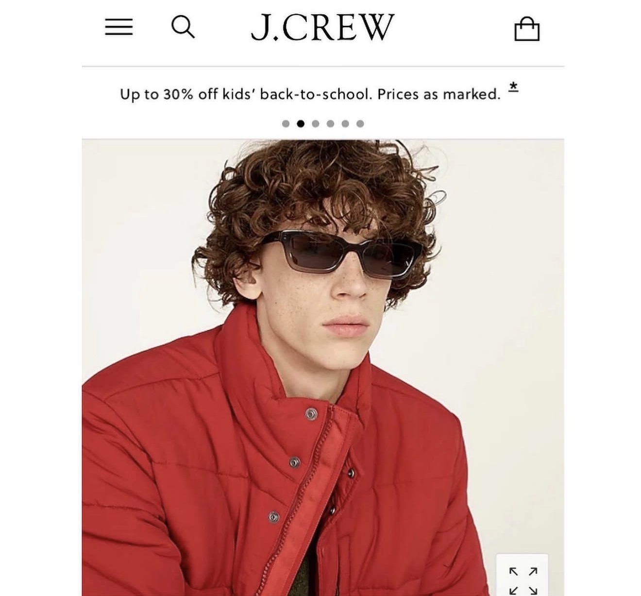 Young person with curly hair wearing sunglasses and a red jacket, facing forward.