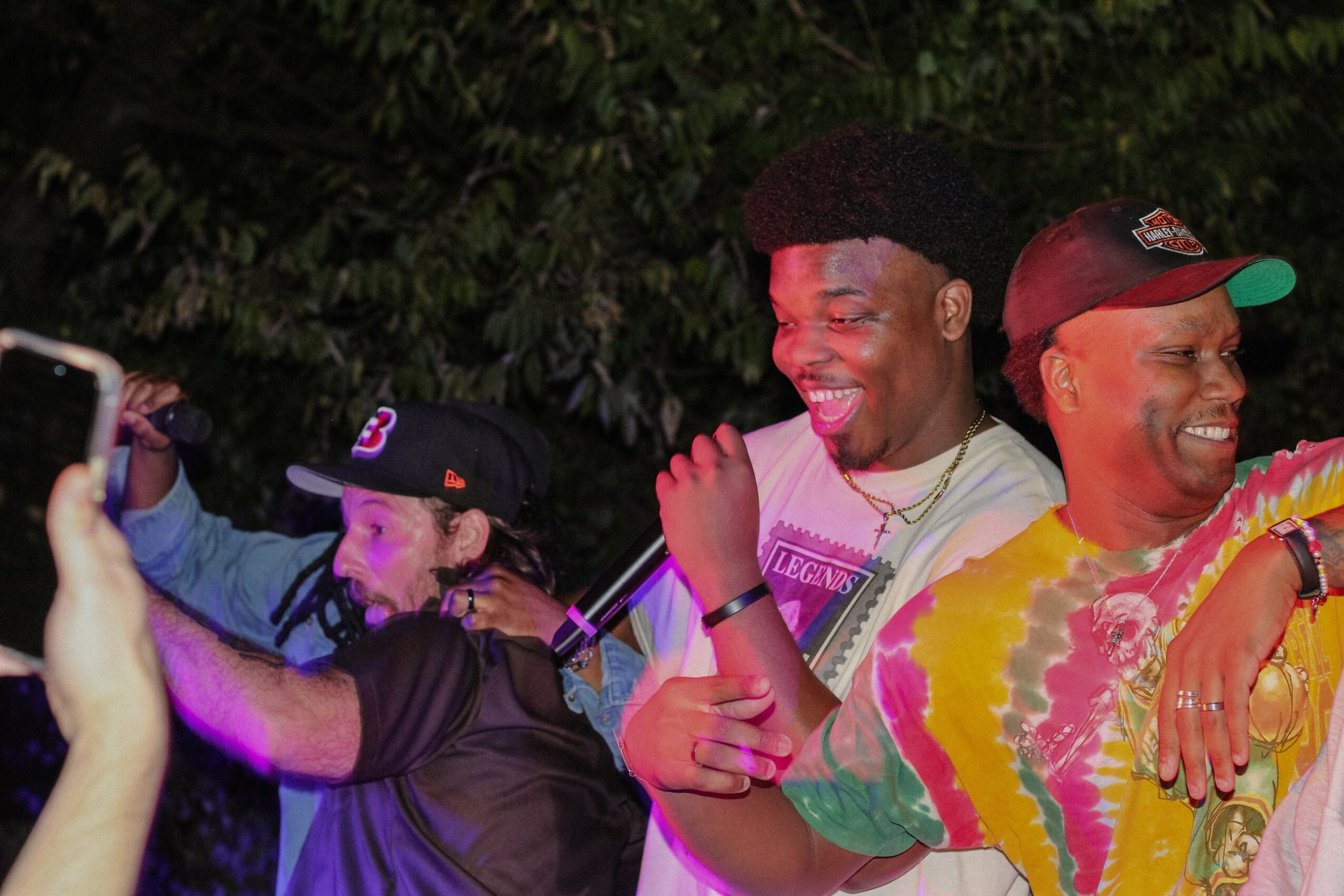 Three people smiling and enjoying a moment outdoors at night, with trees in the background.