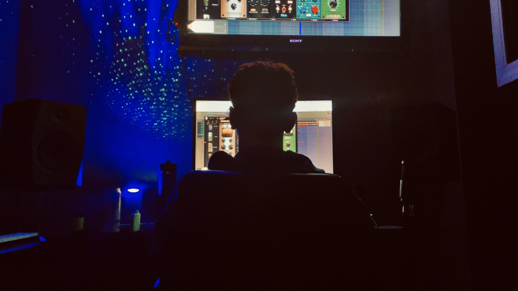 Person sitting in front of multiple computer screens in a dark room with blue lighting.