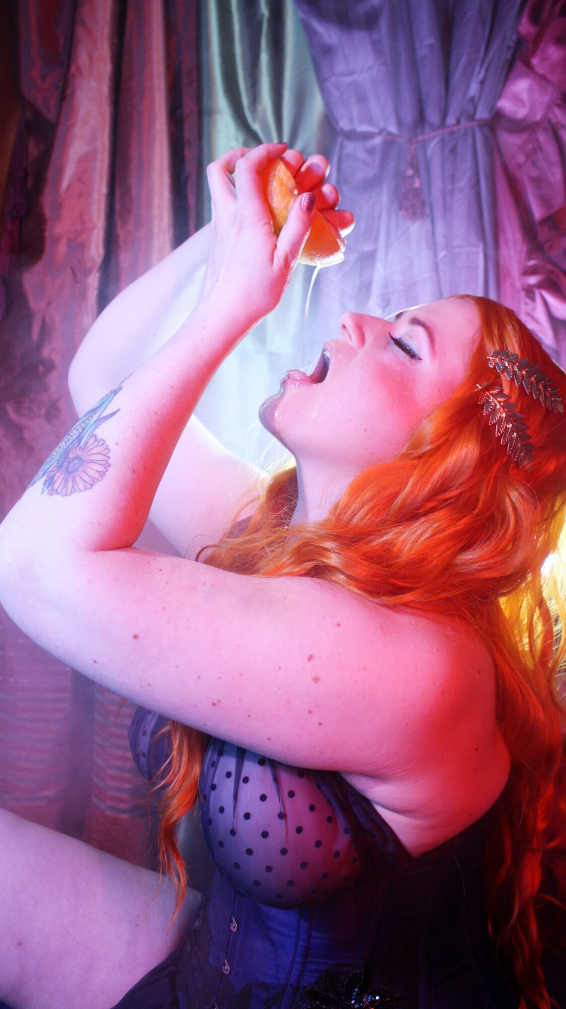 Woman with red hair holding a small object near her face, in front of colorful curtains.