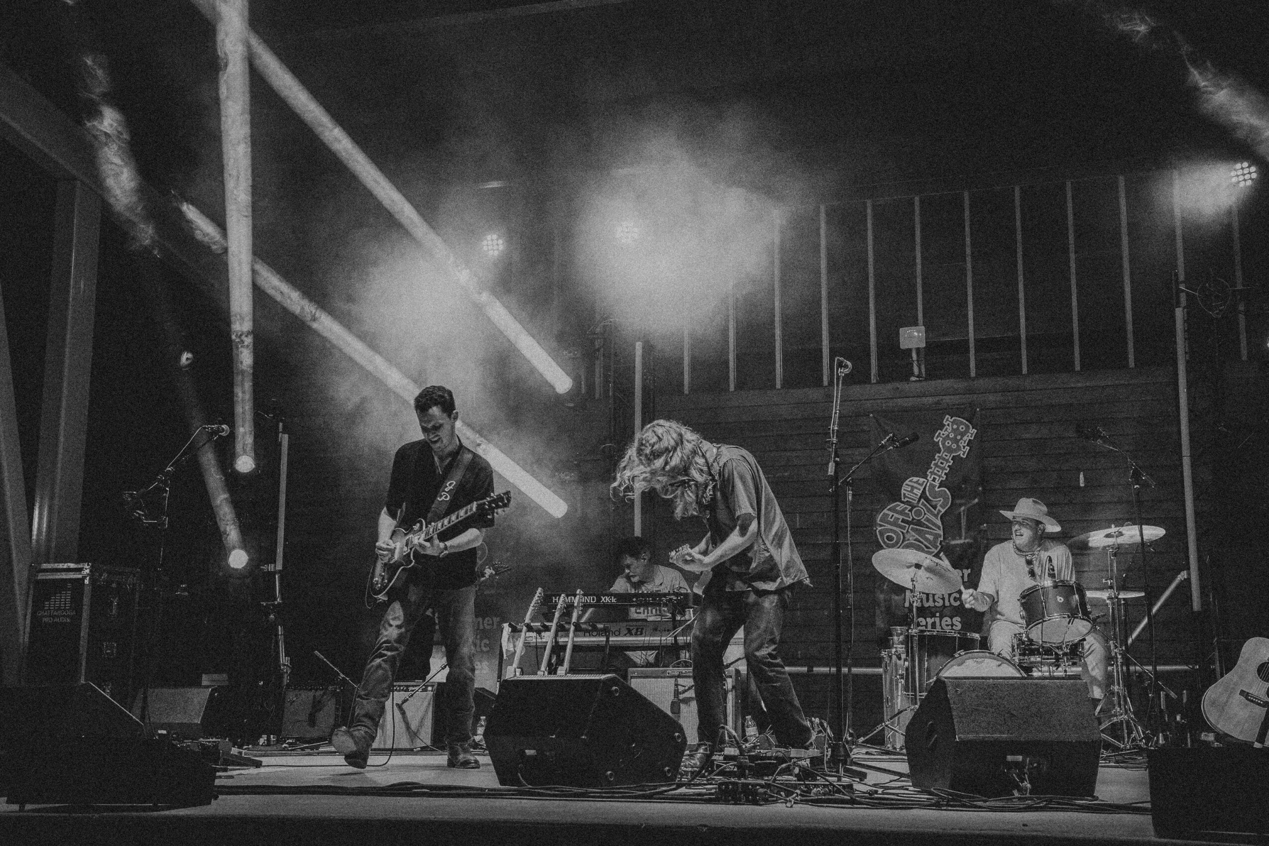Band performing on stage with musicians playing instruments and stage lighting effects, in black and white.