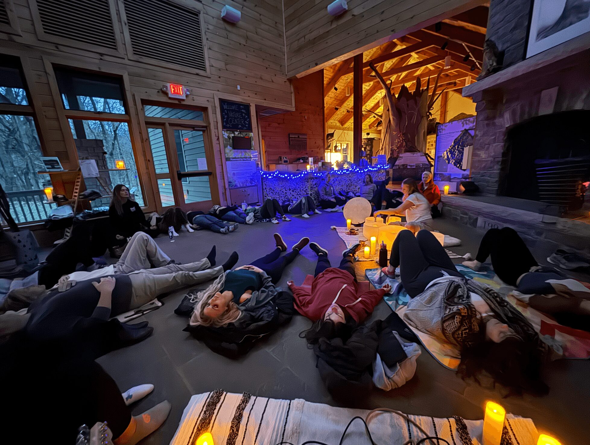 People lying on the floor in a cozy room with a fireplace, decorated with candles and string lights, during evening.