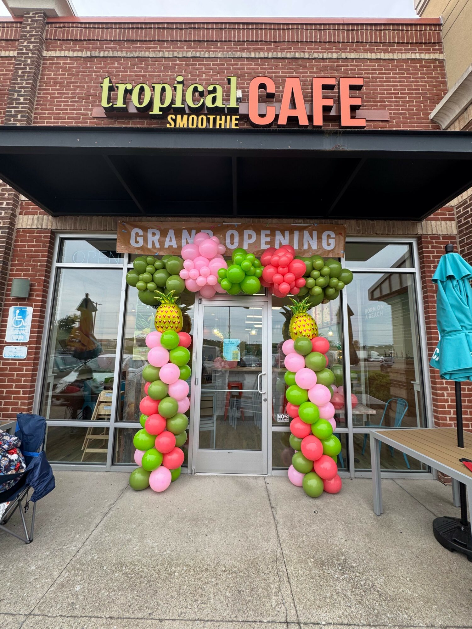 Store entrance decorated with pink, green, and white balloons, with a sign reading 'Grand Opening' and a person inside.