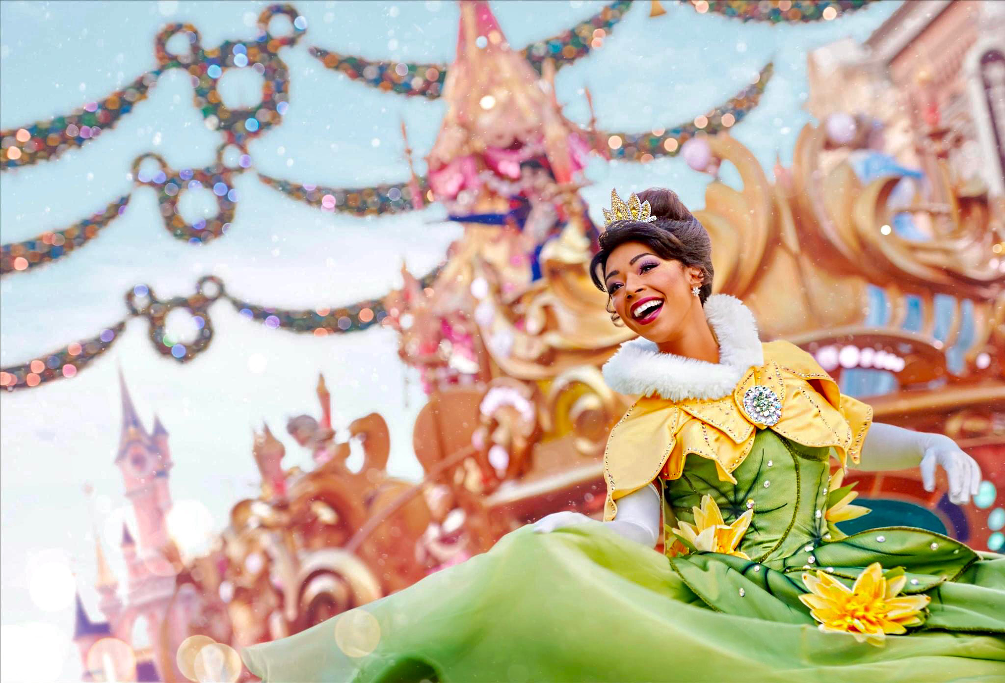 A woman dressed as a princess in a green and yellow costume, smiling on a parade float with a castle background.