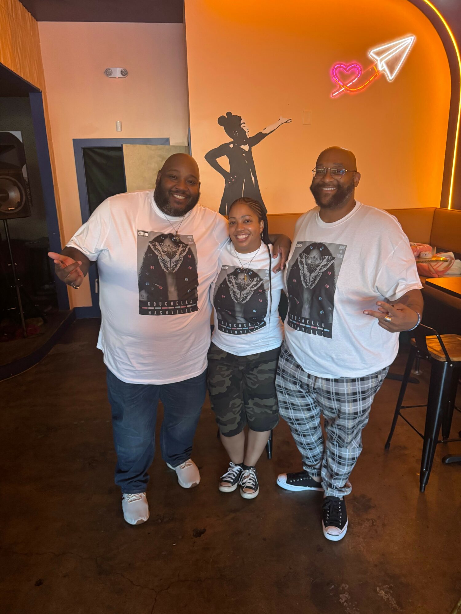 Three people standing together indoors, two men and one woman, with neon lights and a sculpture in the background.