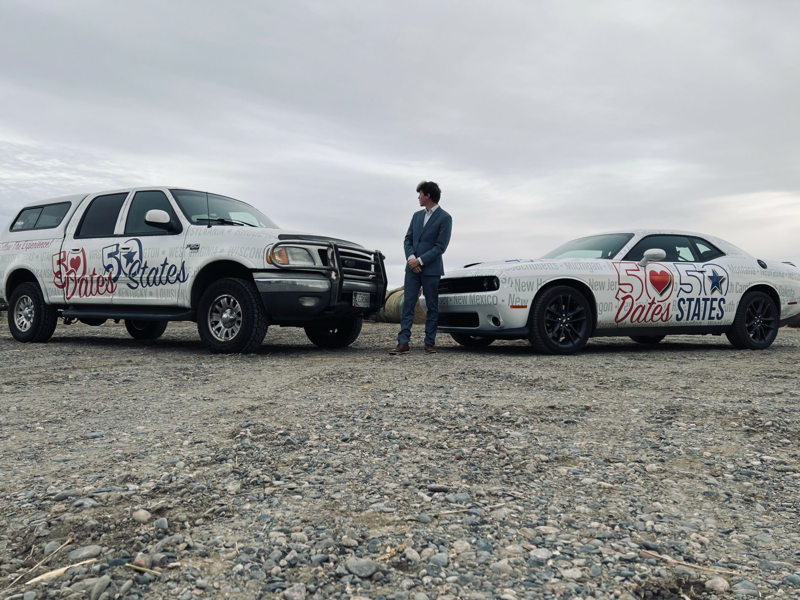 Person standing between two cars with wedding-themed decorations, on a gravel surface under a cloudy sky.