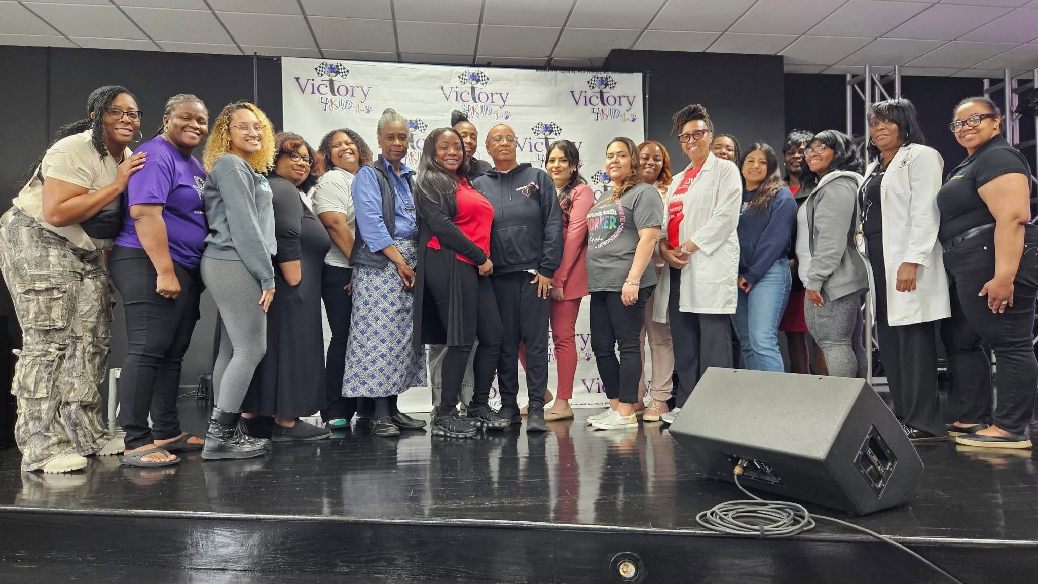 Group of women standing on stage in front of a Victory banner, smiling and posing for a photo.