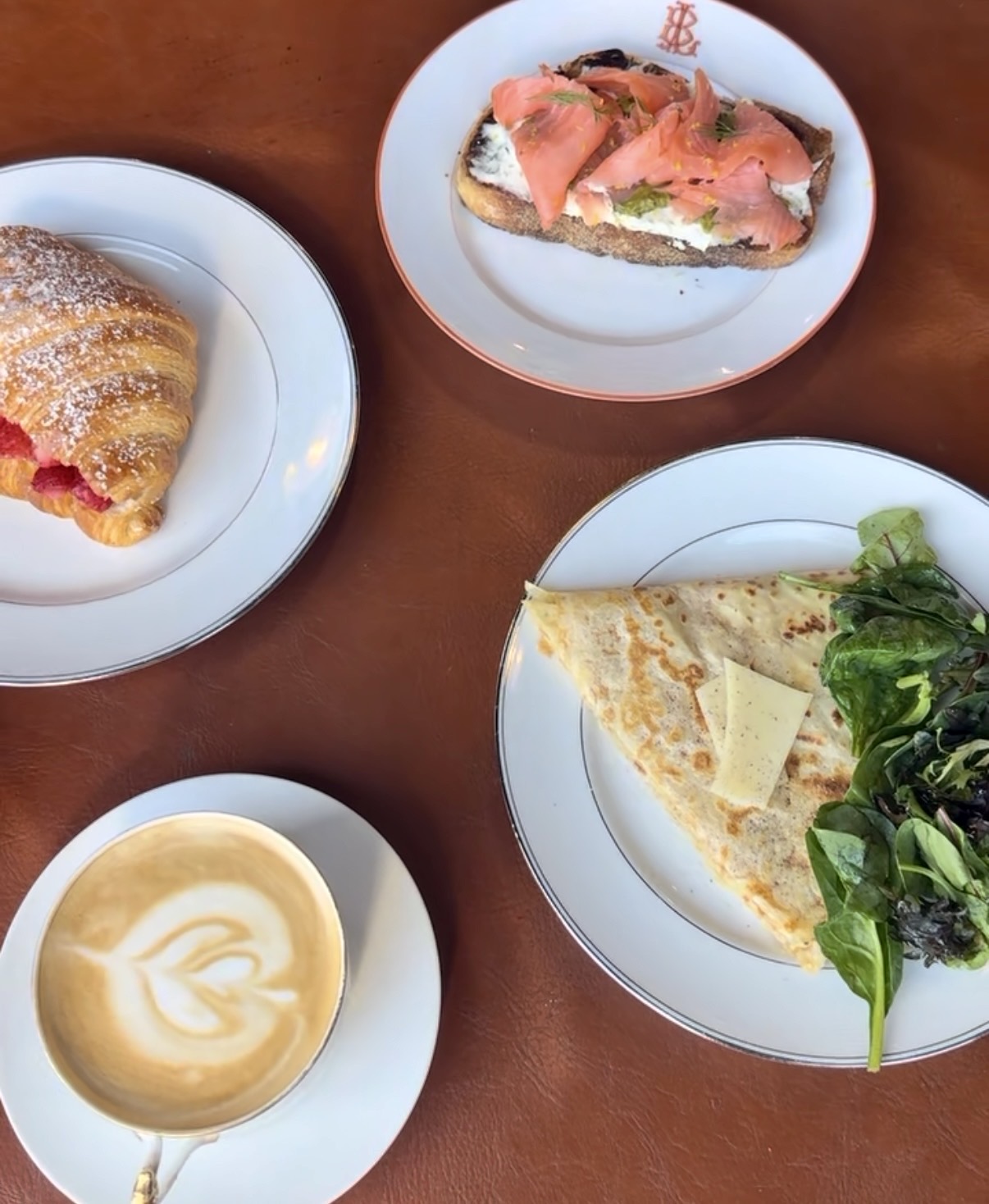 Three plates with different food items and a cup of coffee on a wooden table.