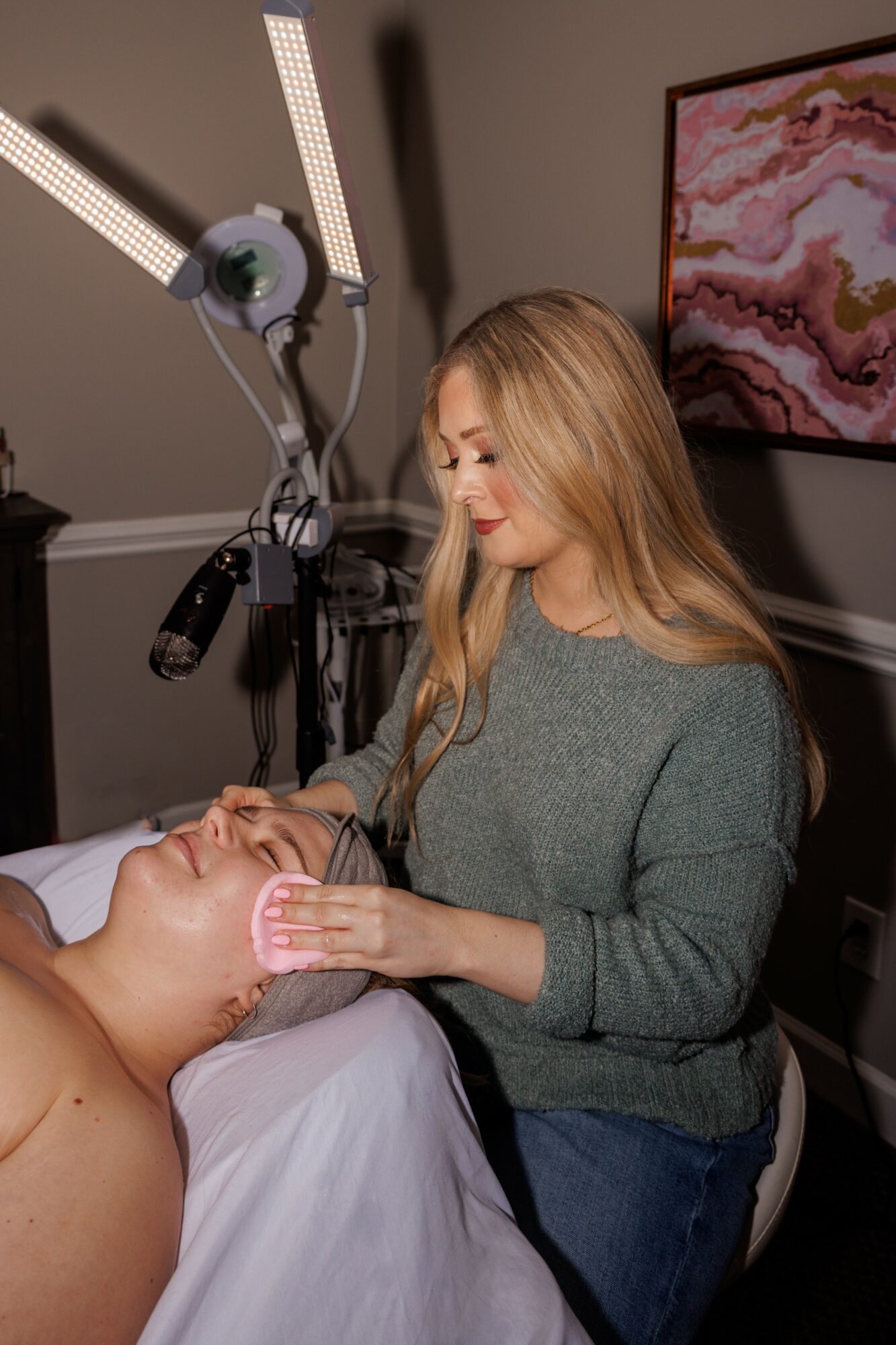 Woman receiving facial treatment in a spa or clinic, with a professional applying a mask or cream to her face.