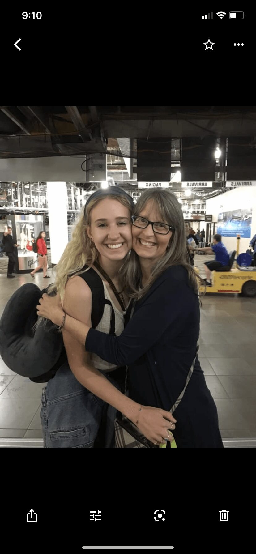 Two women hugging and smiling in an indoor setting with a yellow vehicle in the background.