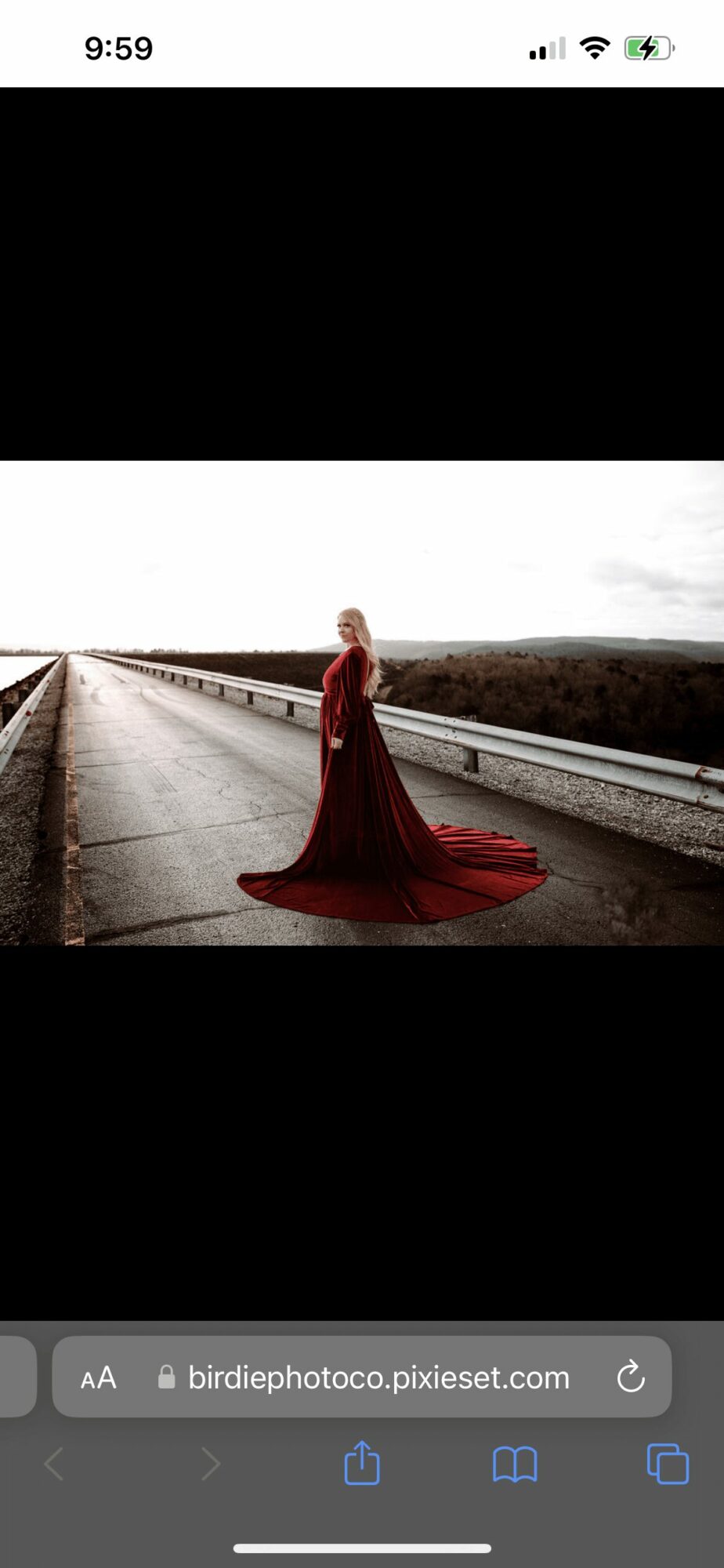Person in a long red dress standing on an empty road with a cloudy sky, landscape in the background.