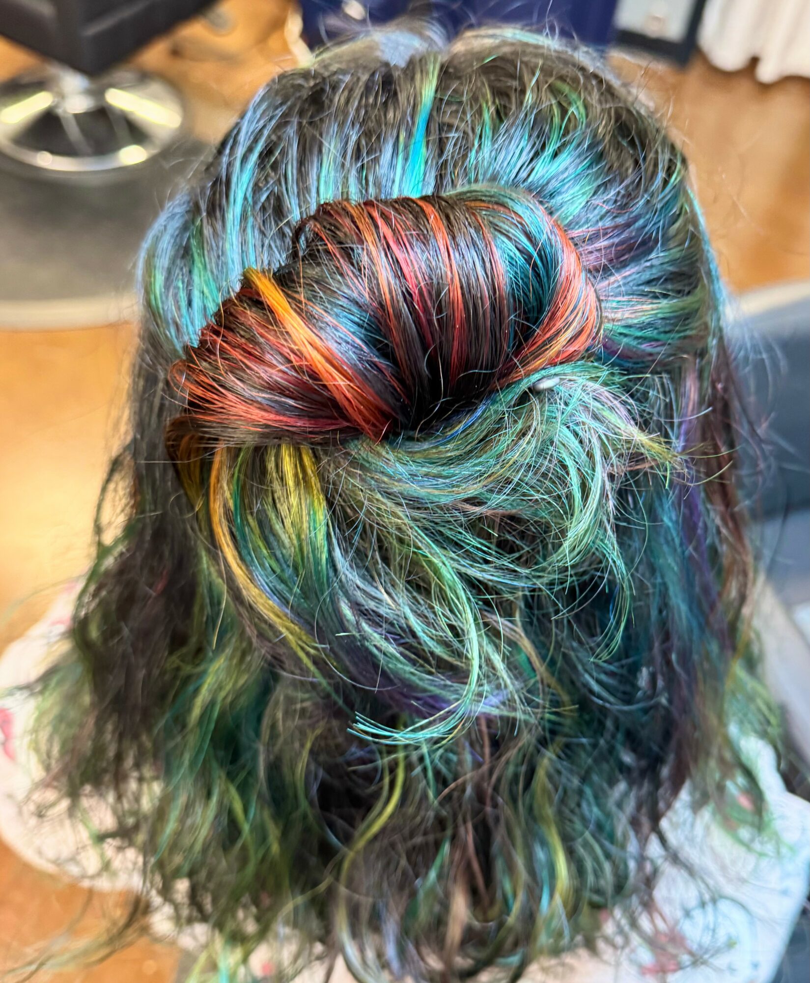 Person's hair styled in a bun with multicolored rainbow highlights and wavy texture, viewed from above.