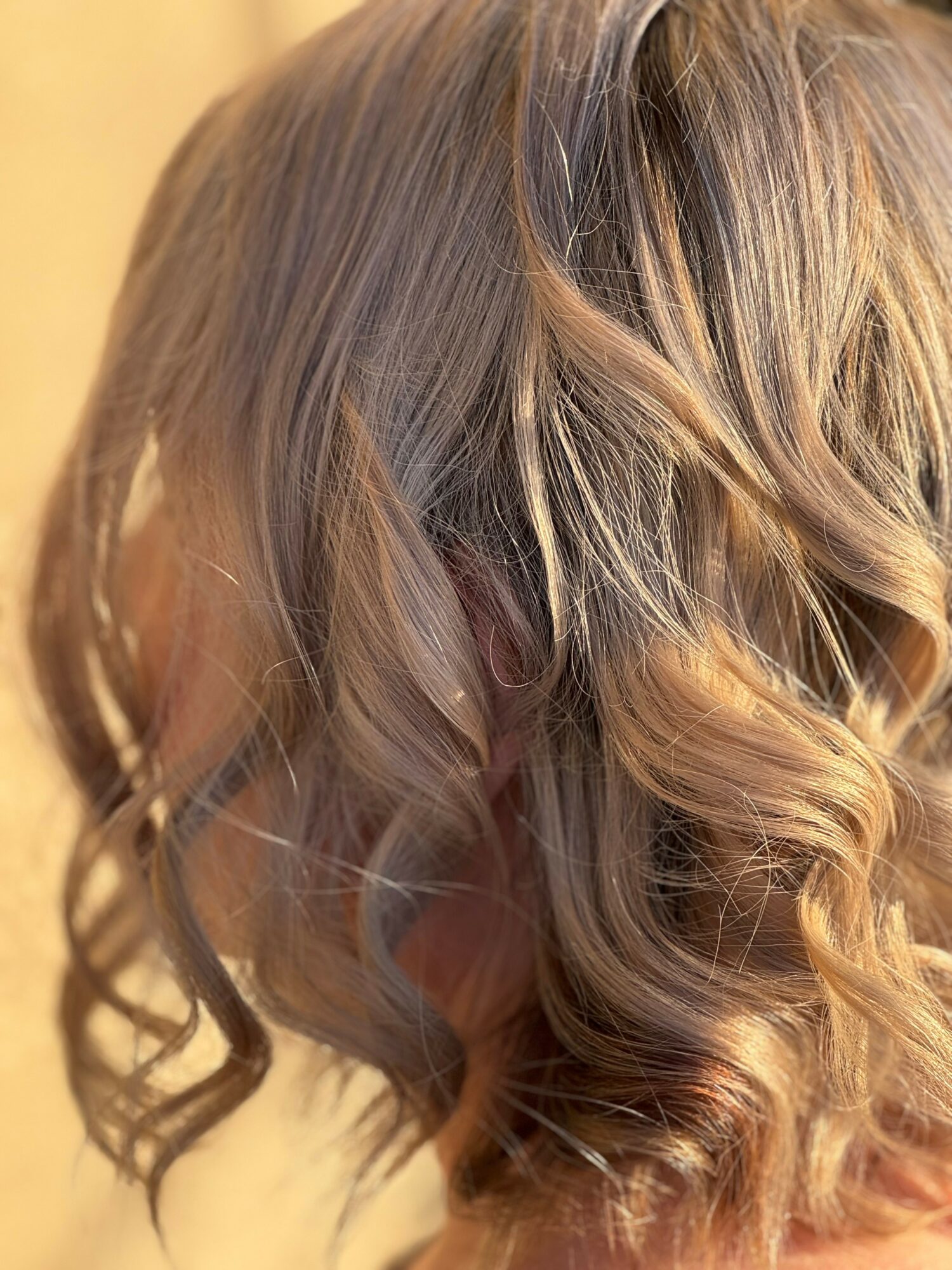 Close-up of a person's wavy, blonde hair with highlights, styled in loose curls.