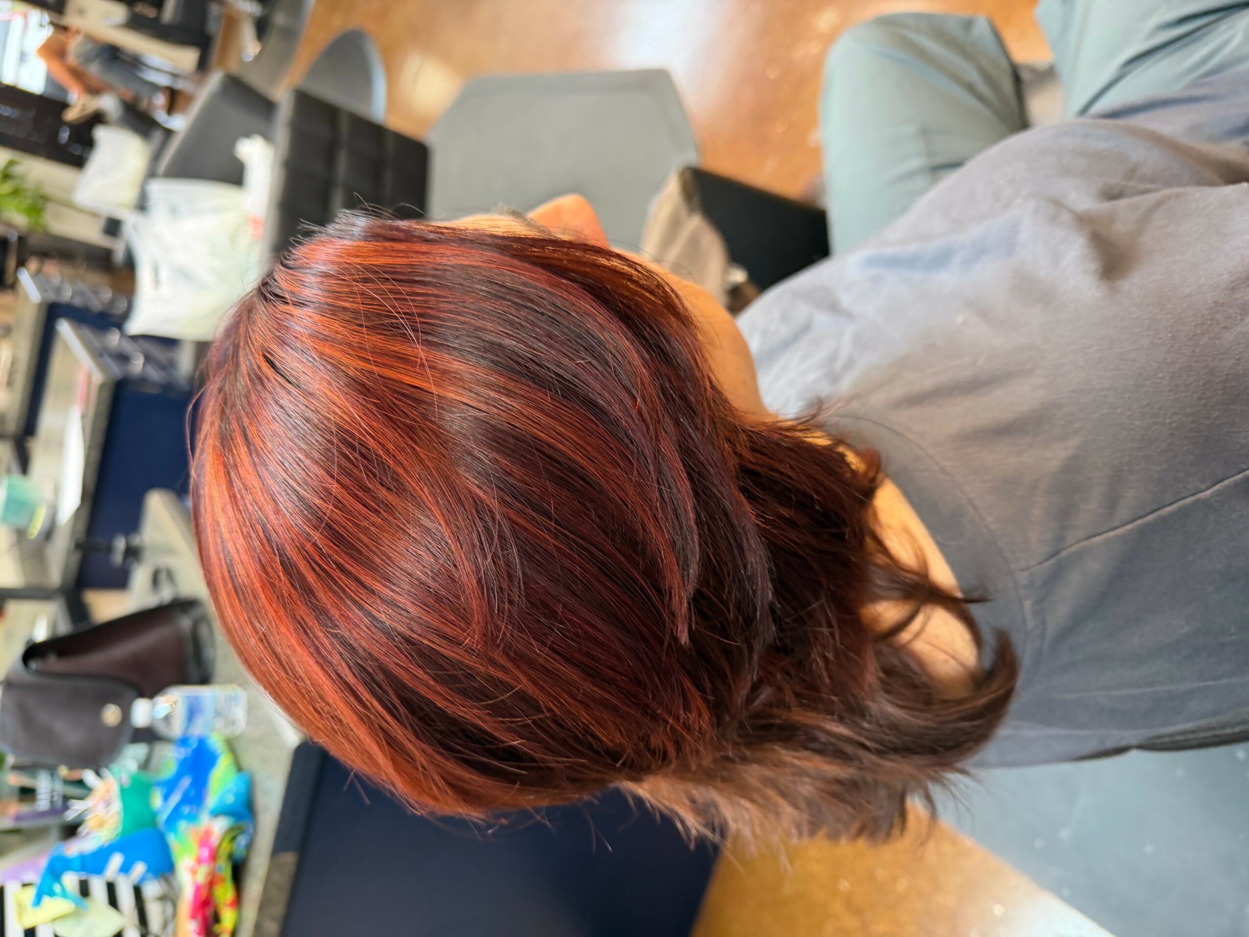 Person with shoulder-length red hair sitting in a room with chairs and tables, facing away from the camera.