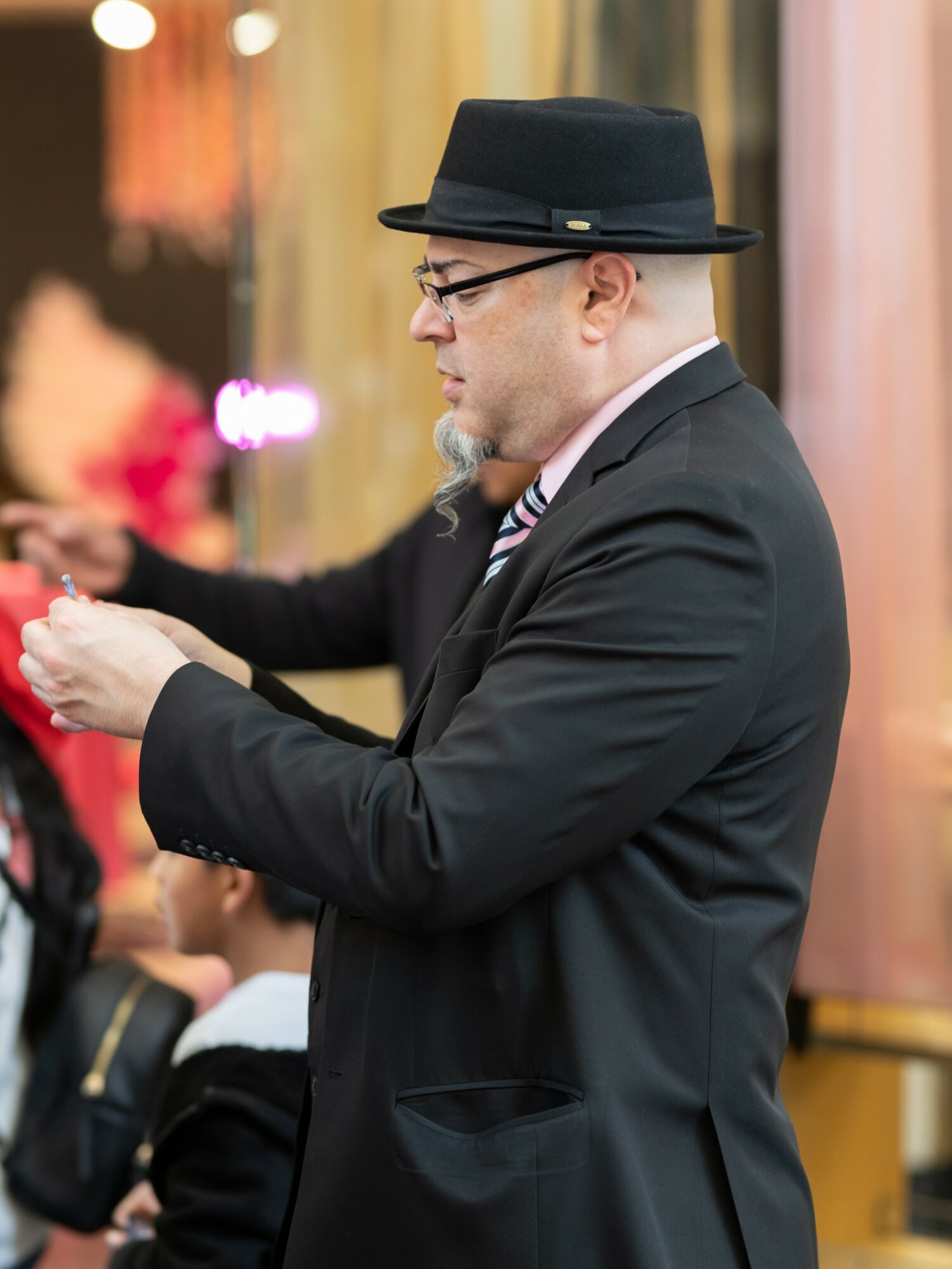 Man in suit and hat looking at his phone in an indoor setting with blurred background