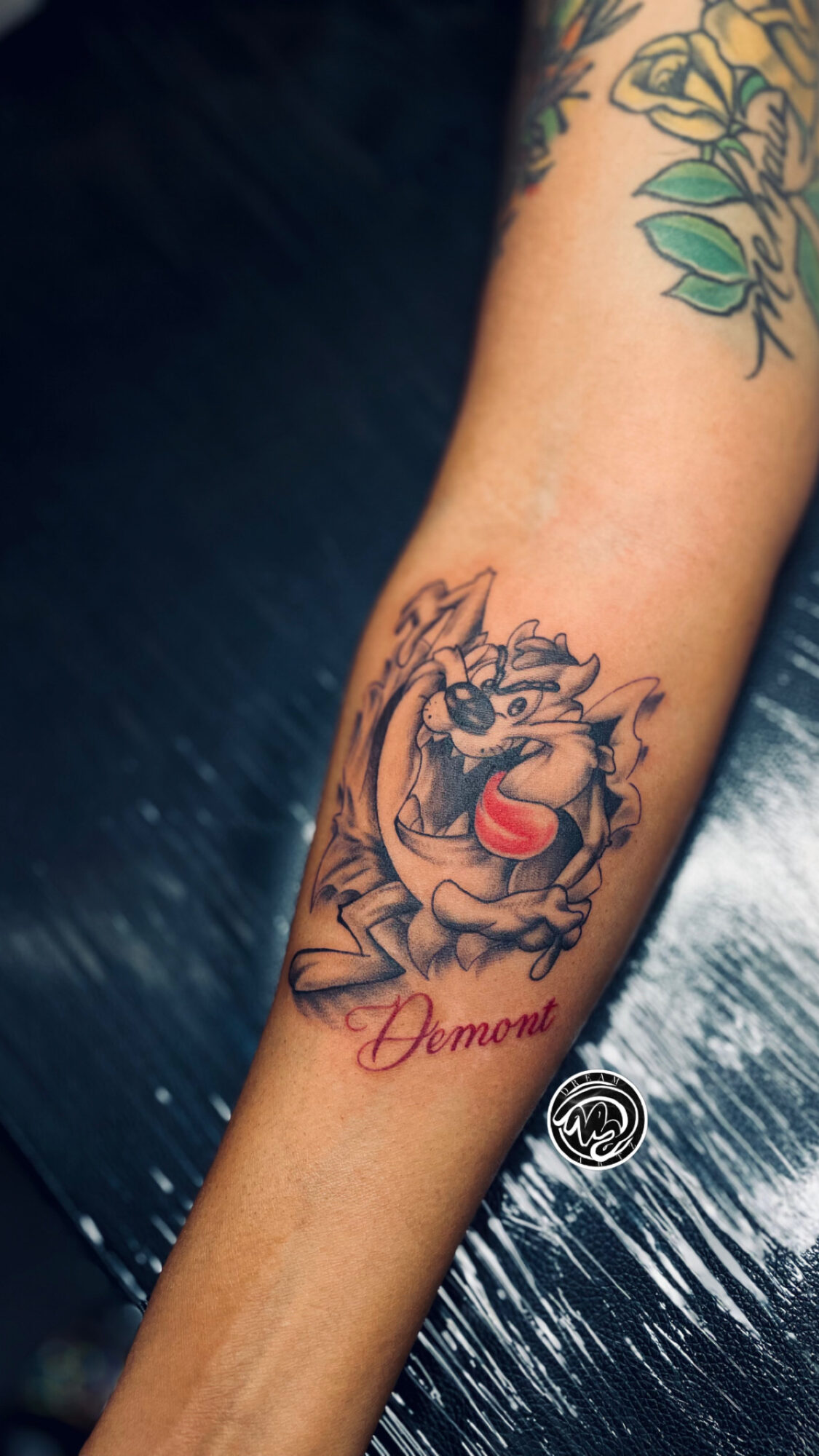 Tattoo of a cartoonish dragon with an open mouth and a red tongue, and the word 'Mommy' below it.