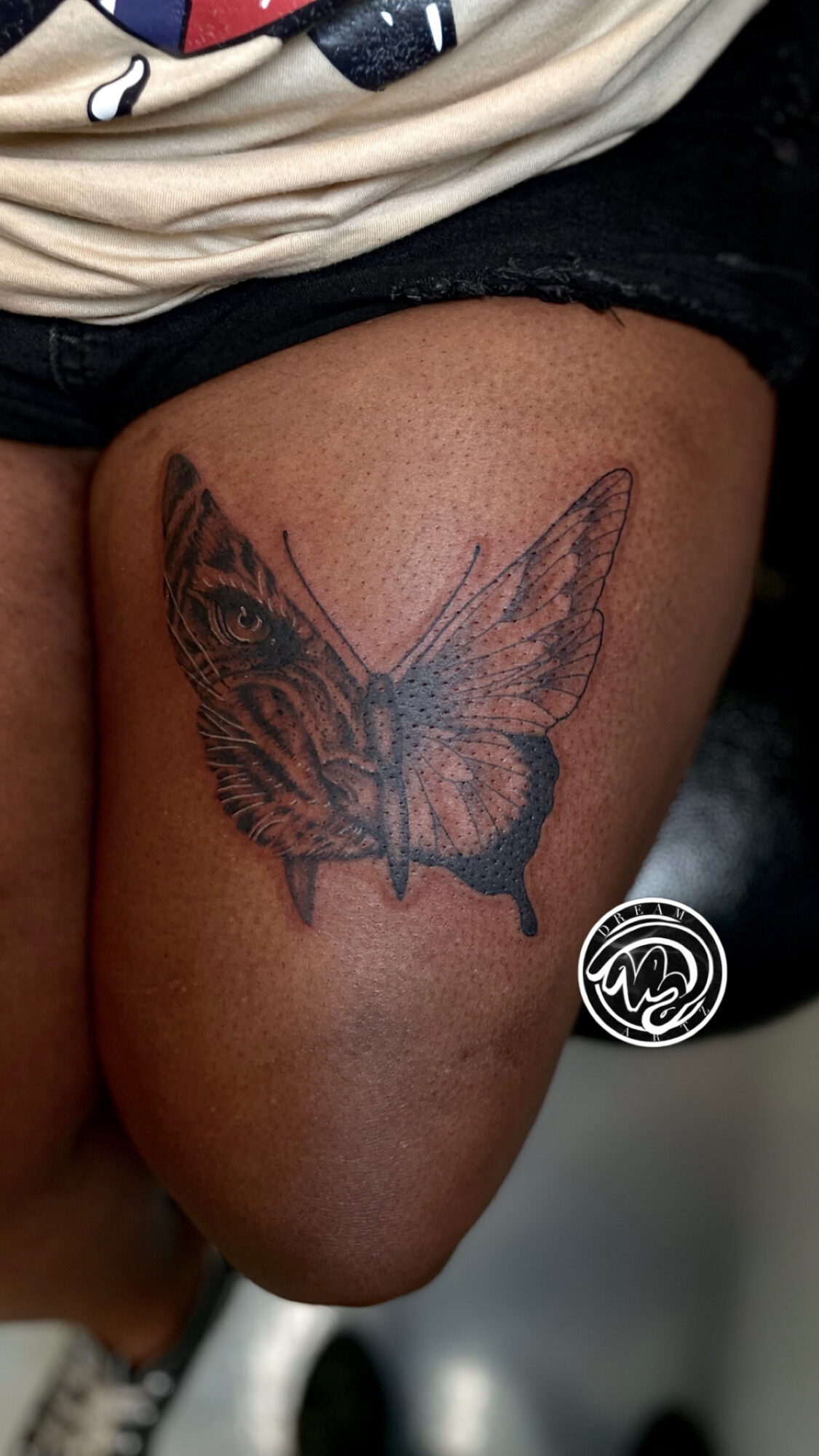 Tattoo of a butterfly on a person's thigh, with detailed wings and body, in black ink.