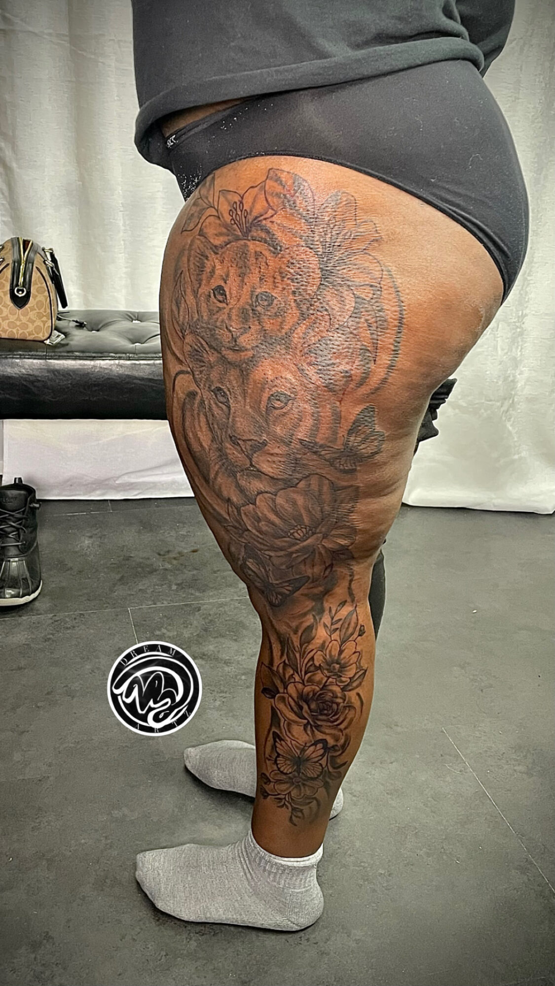 Side view of a person with a large tattoo covering the thigh and hip area, wearing black shorts and gray socks.