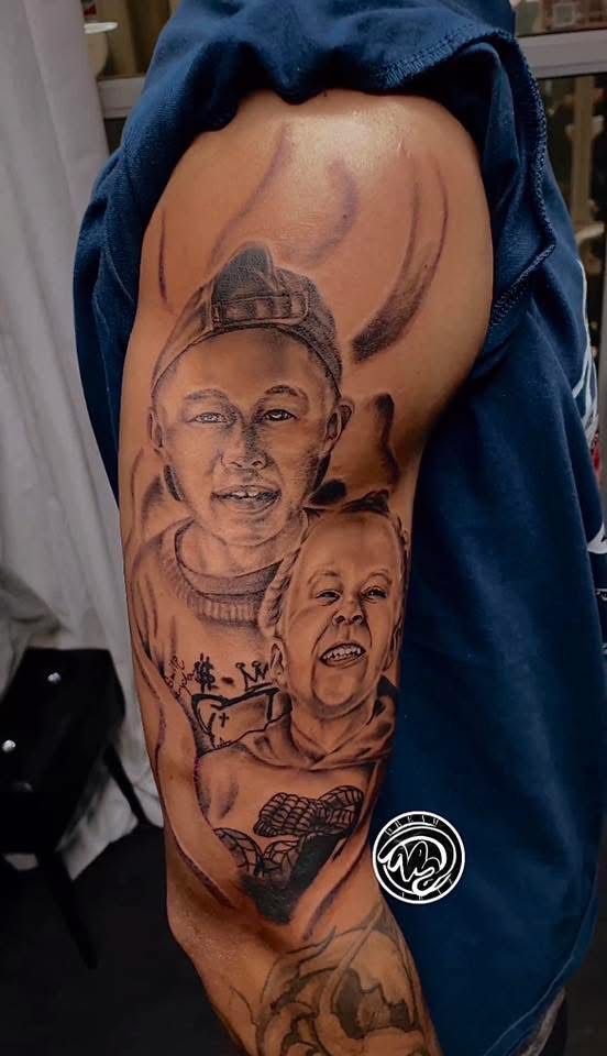 Tattoo of two women, one with a bun and glasses, and the other with short hair, on person's upper arm.