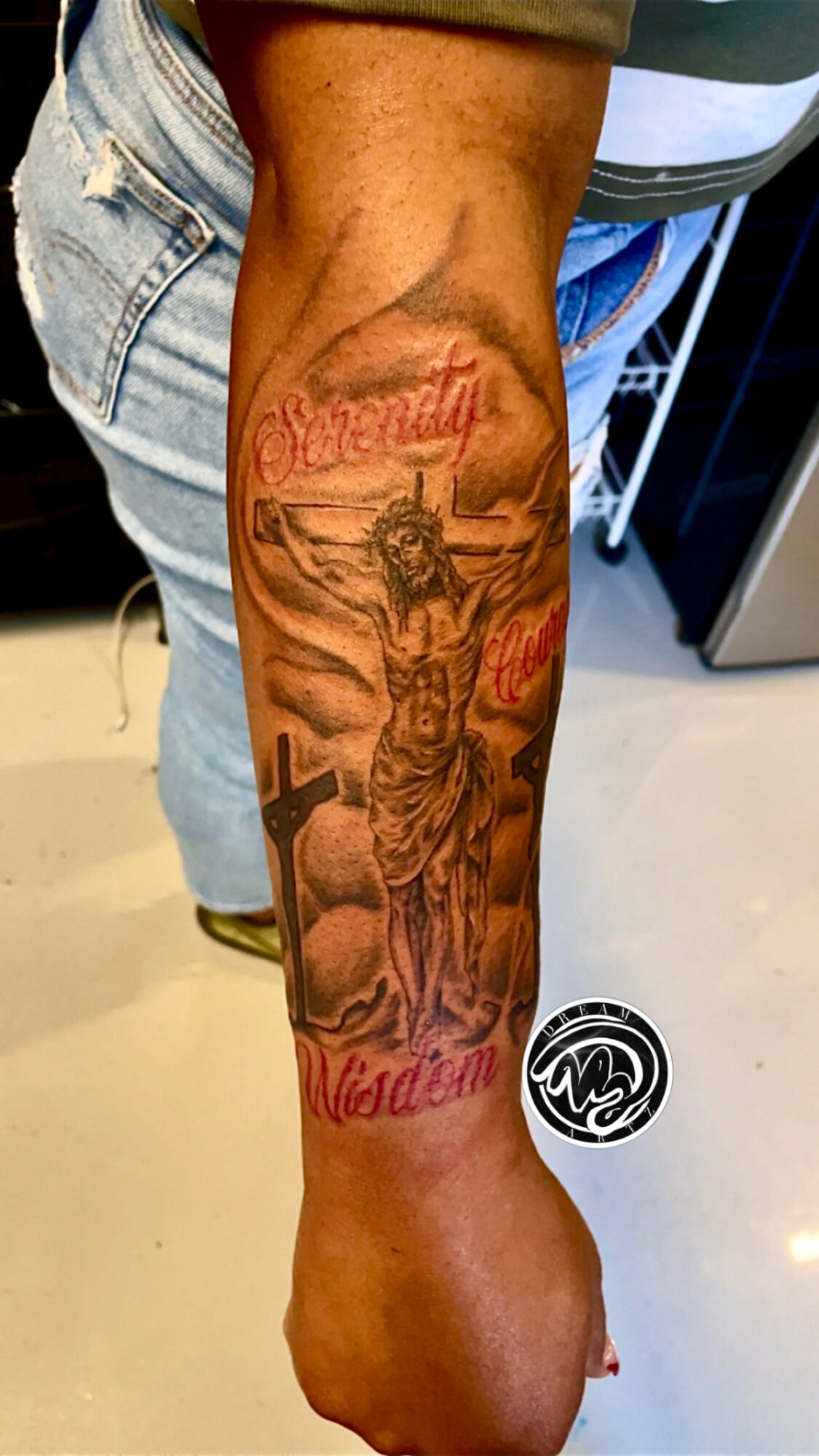 Tattoo of the Statue of Liberty on person's forearm with red script text above and below.