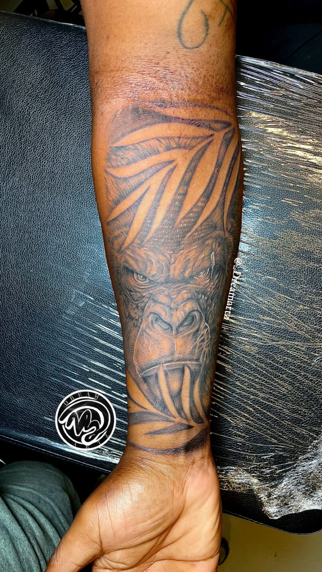 Forearm tattoo featuring a large, detailed lion's face with a mane, and decorative leaf patterns above it.