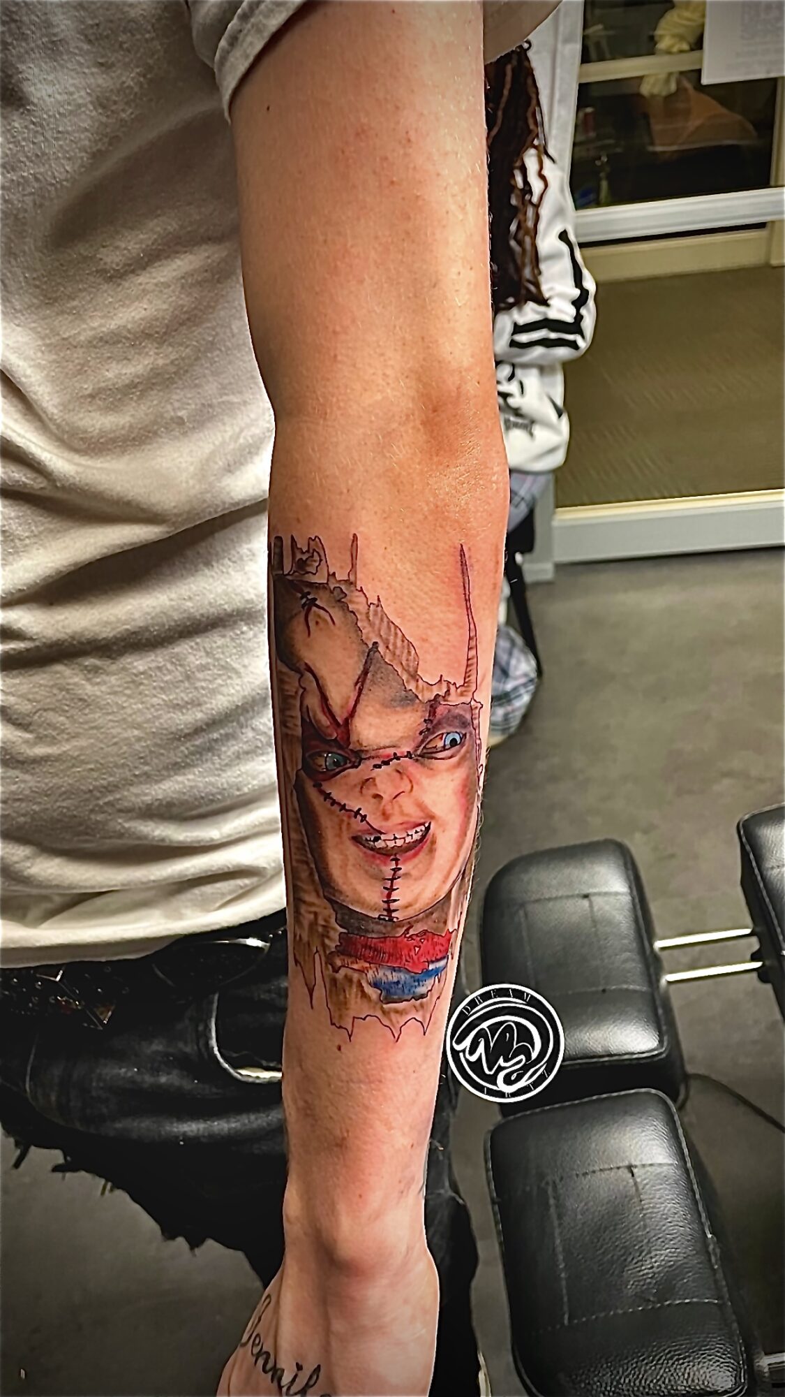 Forearm tattoo of a woman's face with long hair, detailed and colorful, with a background of abstract elements.