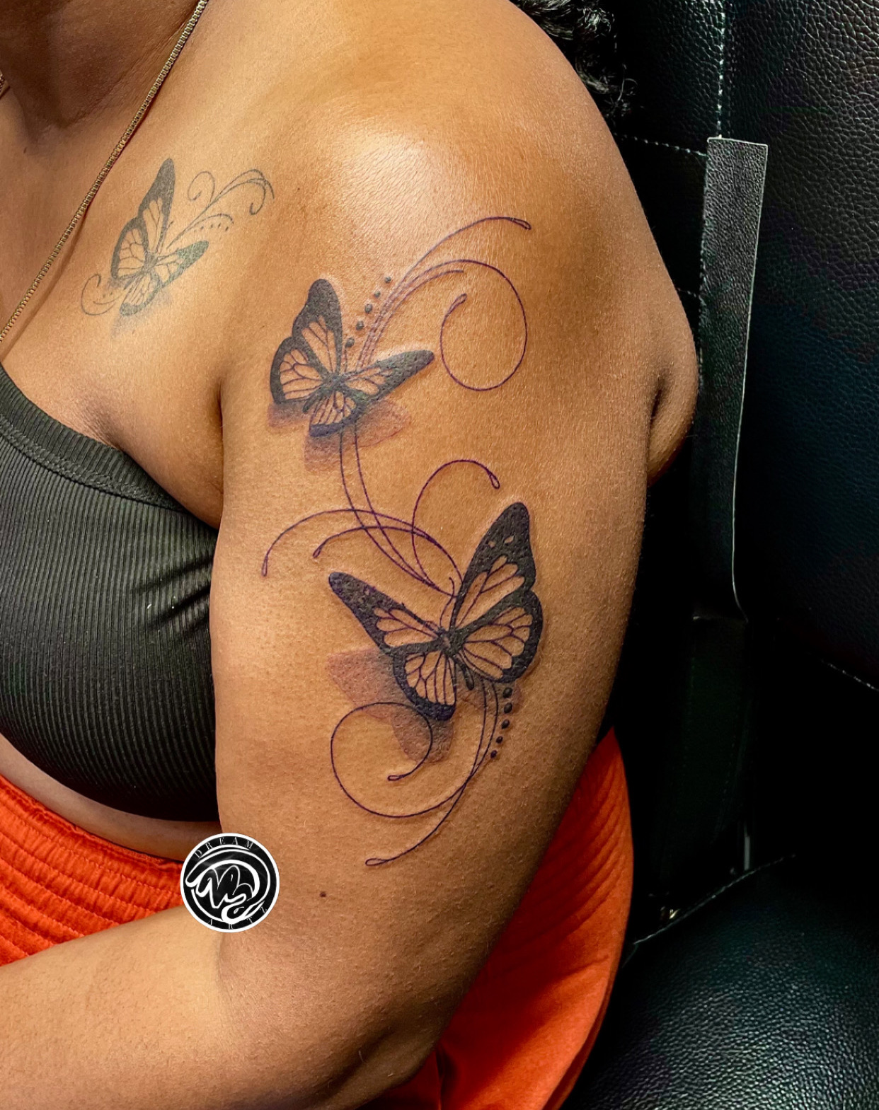 Tattoo of three butterflies with swirling lines on person's upper arm and shoulder, with a black background.