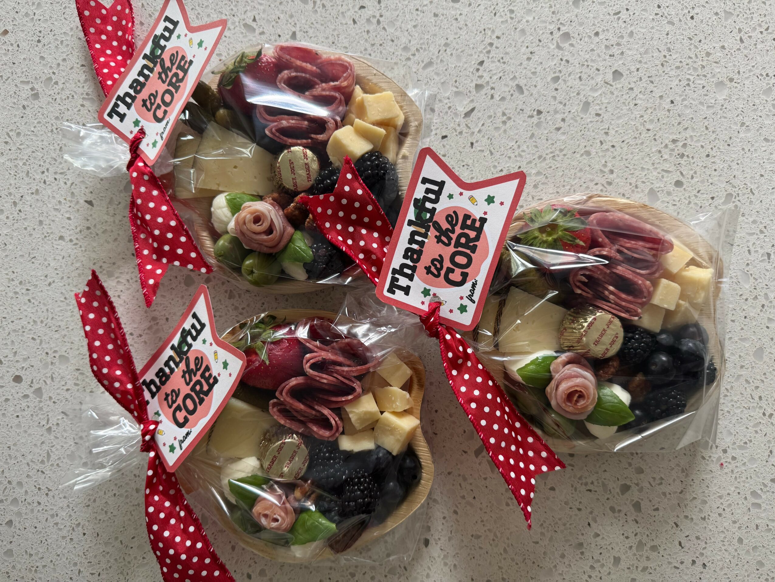 Three small gift bags filled with candies, decorated with red polka dot ribbons and thank you tags, on a light surface.