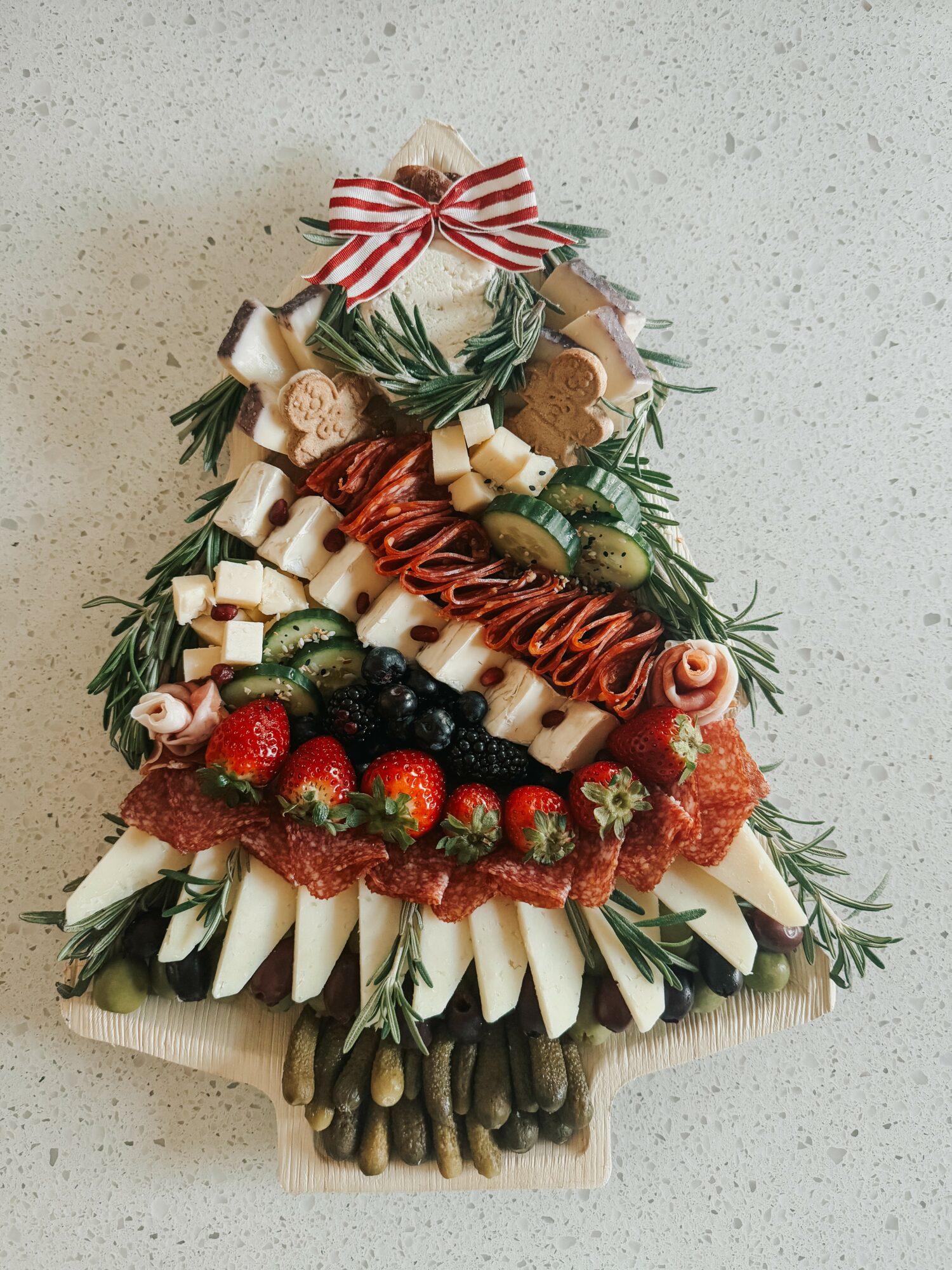 Decorative Christmas tree made of vegetables, strawberries, and herbs with a red and white bow on top.