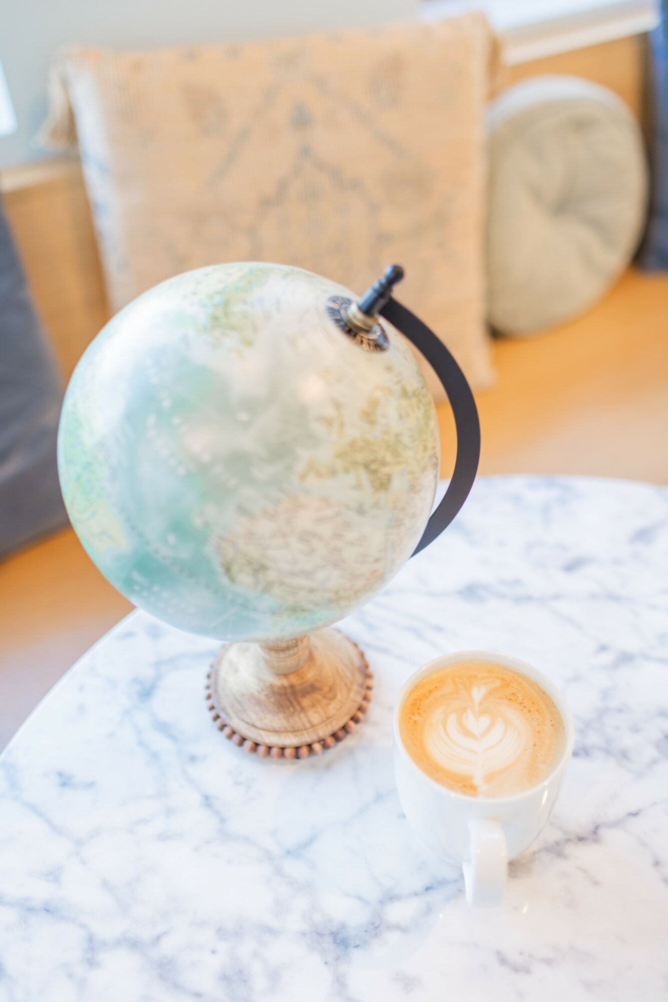 Globe with a black stand on a marble table, with a coffee cup nearby, in a room with beige cushions in the background.