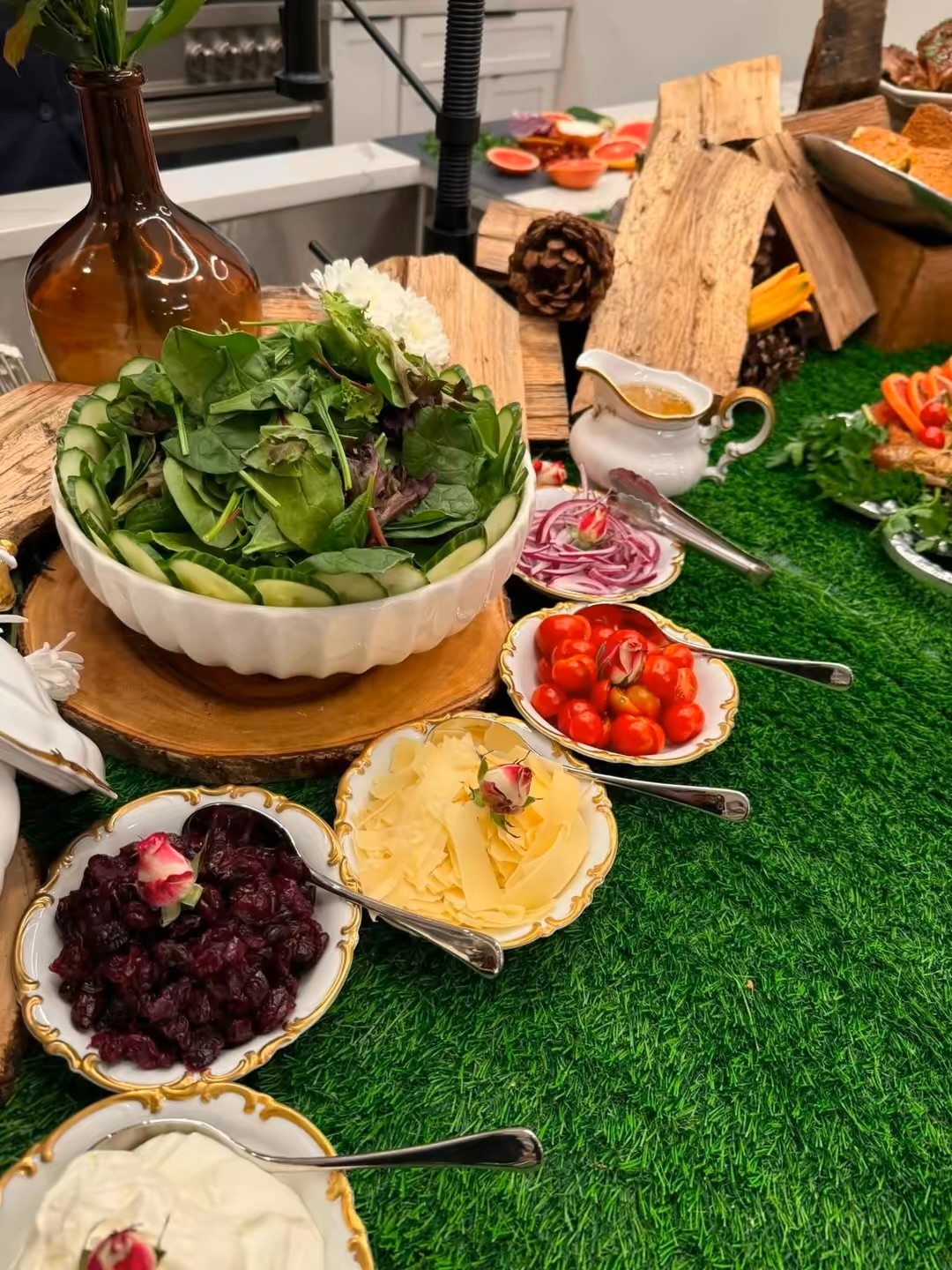 Salad bowl, cherry tomatoes, mashed potatoes, and other dishes on a green tablecloth with decorative items in the background.