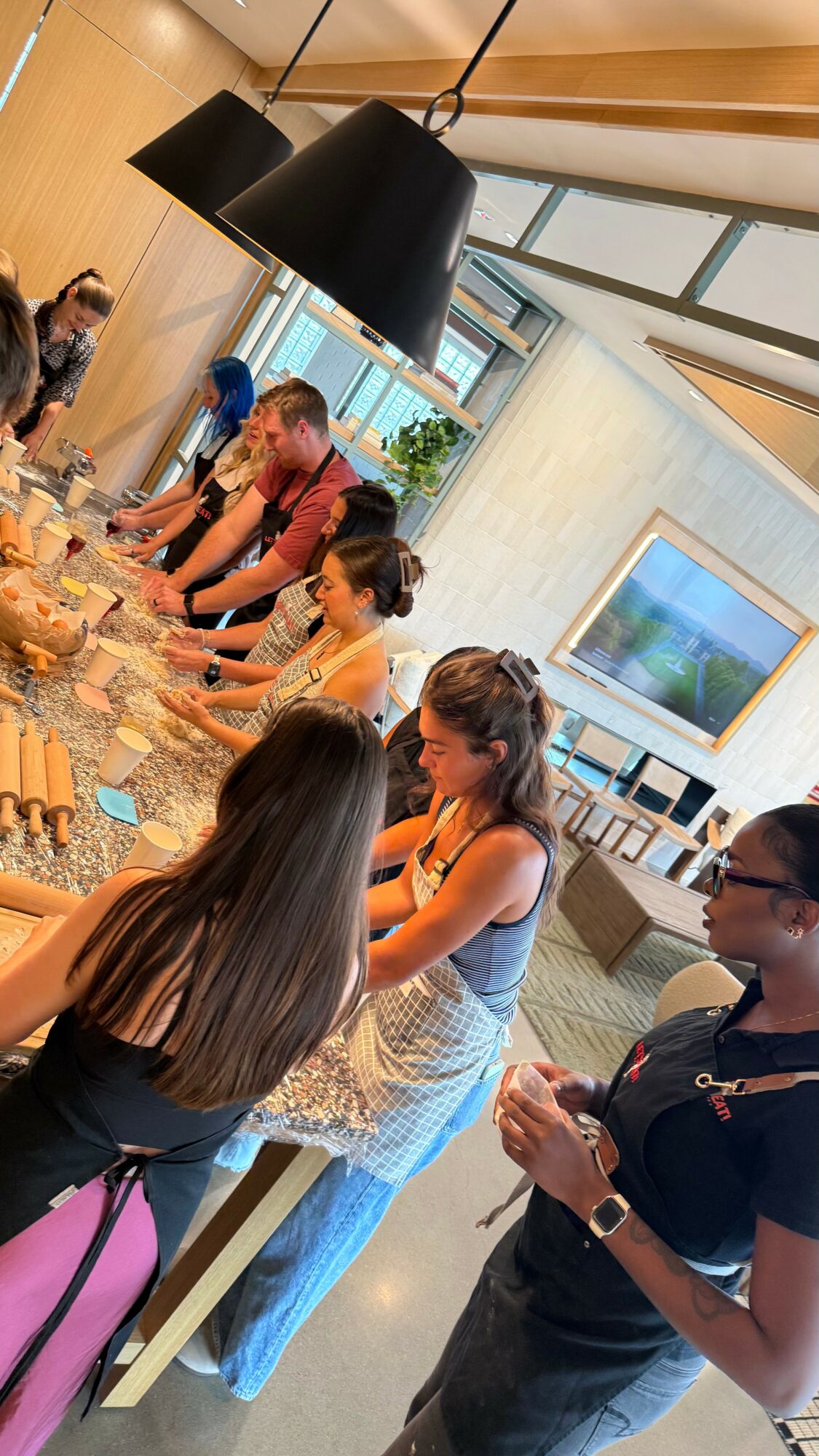 People gathered around a table with food and drinks in a modern indoor space, some engaging in conversation.