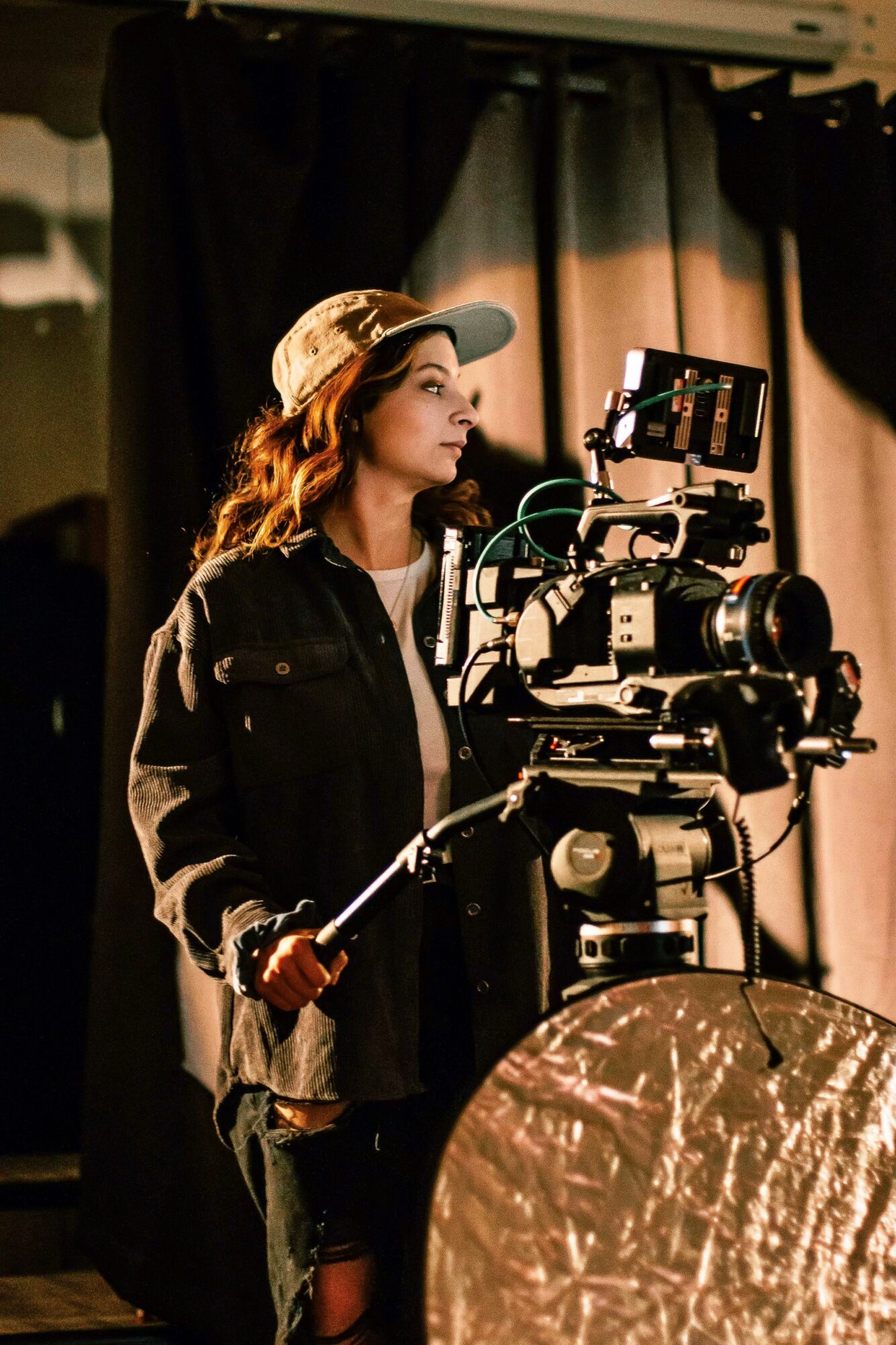 Woman operating professional video camera with lighting equipment in background.