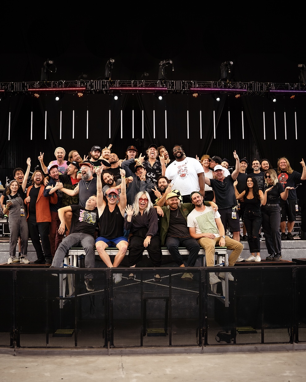 Group of people on stage, some sitting and some standing, with stage lights and equipment in the background.