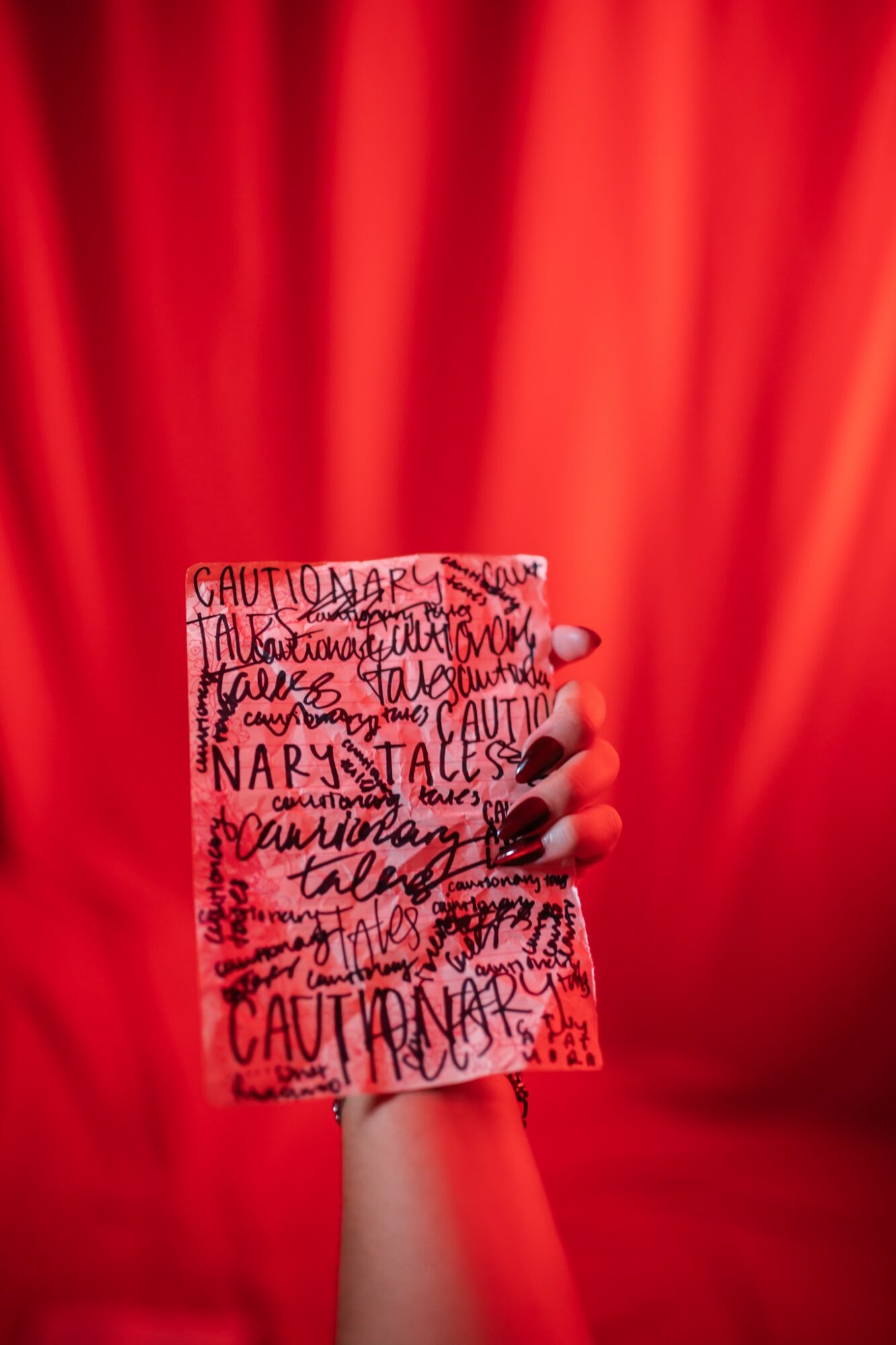 A hand holding a card with warning text, against a red curtain background.