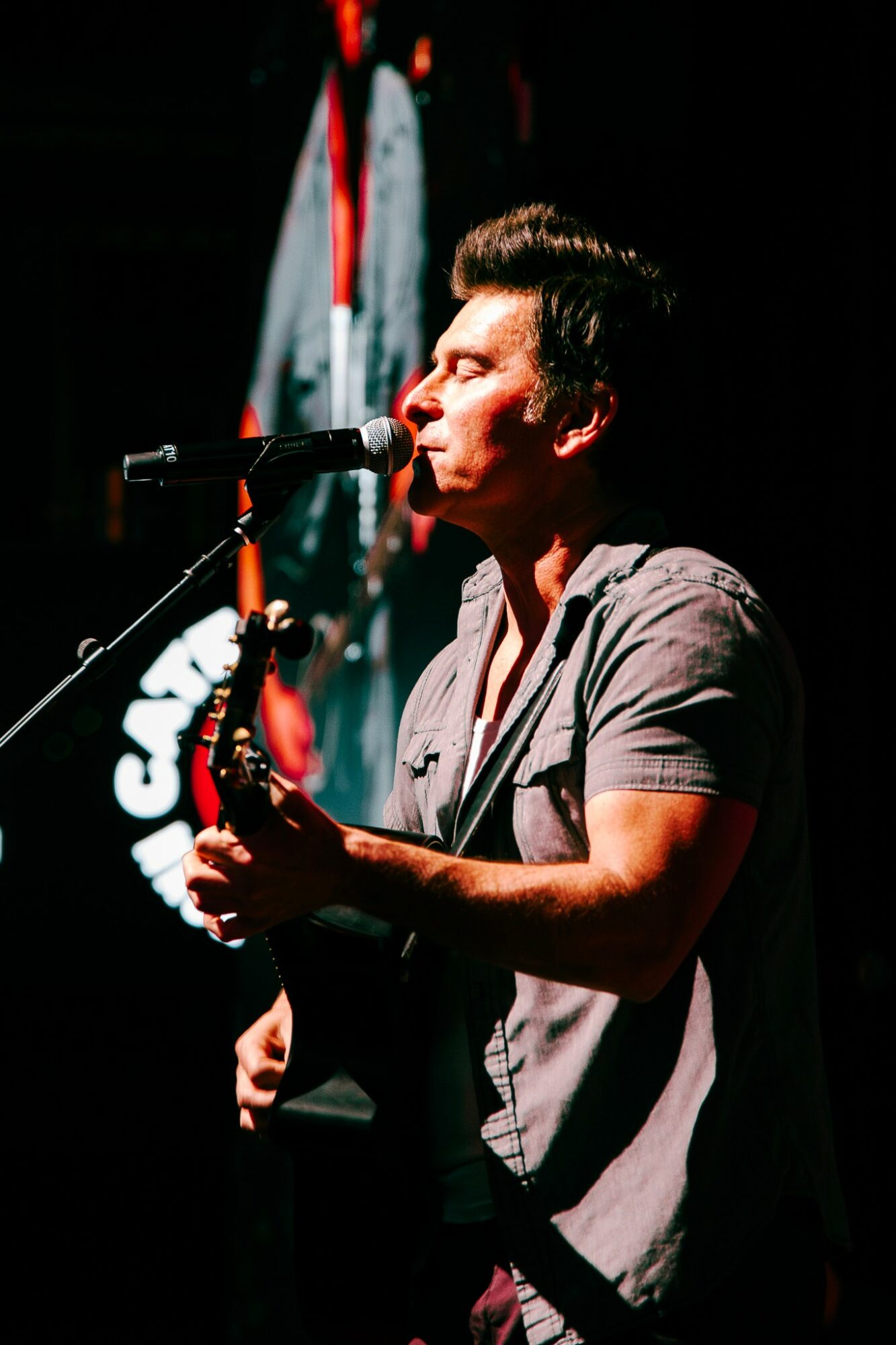 Person playing a wind instrument on stage with a microphone, dark background, and a screen behind them.