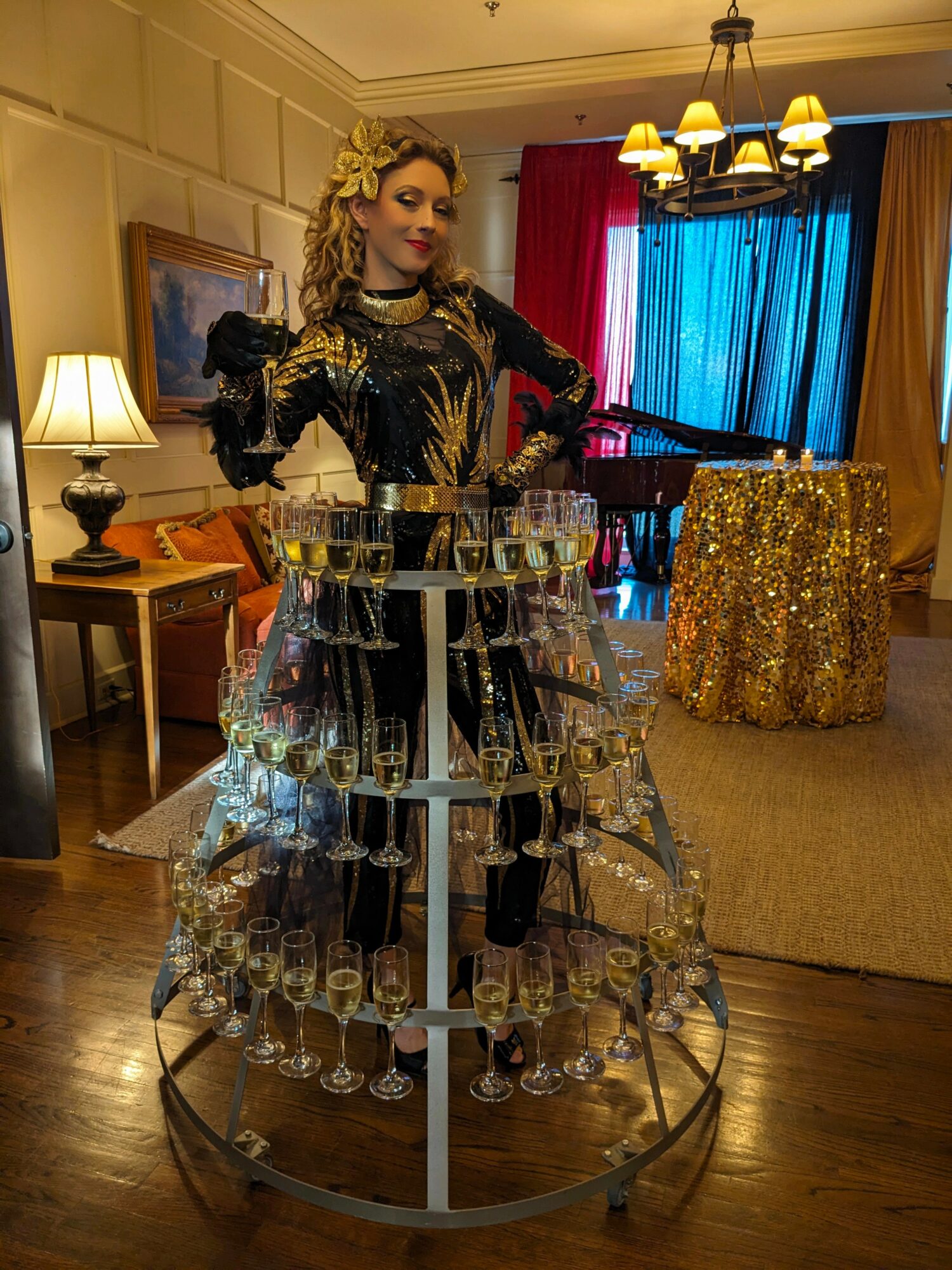 Person in a gold and black outfit stands behind a glassware display in a decorated room.
