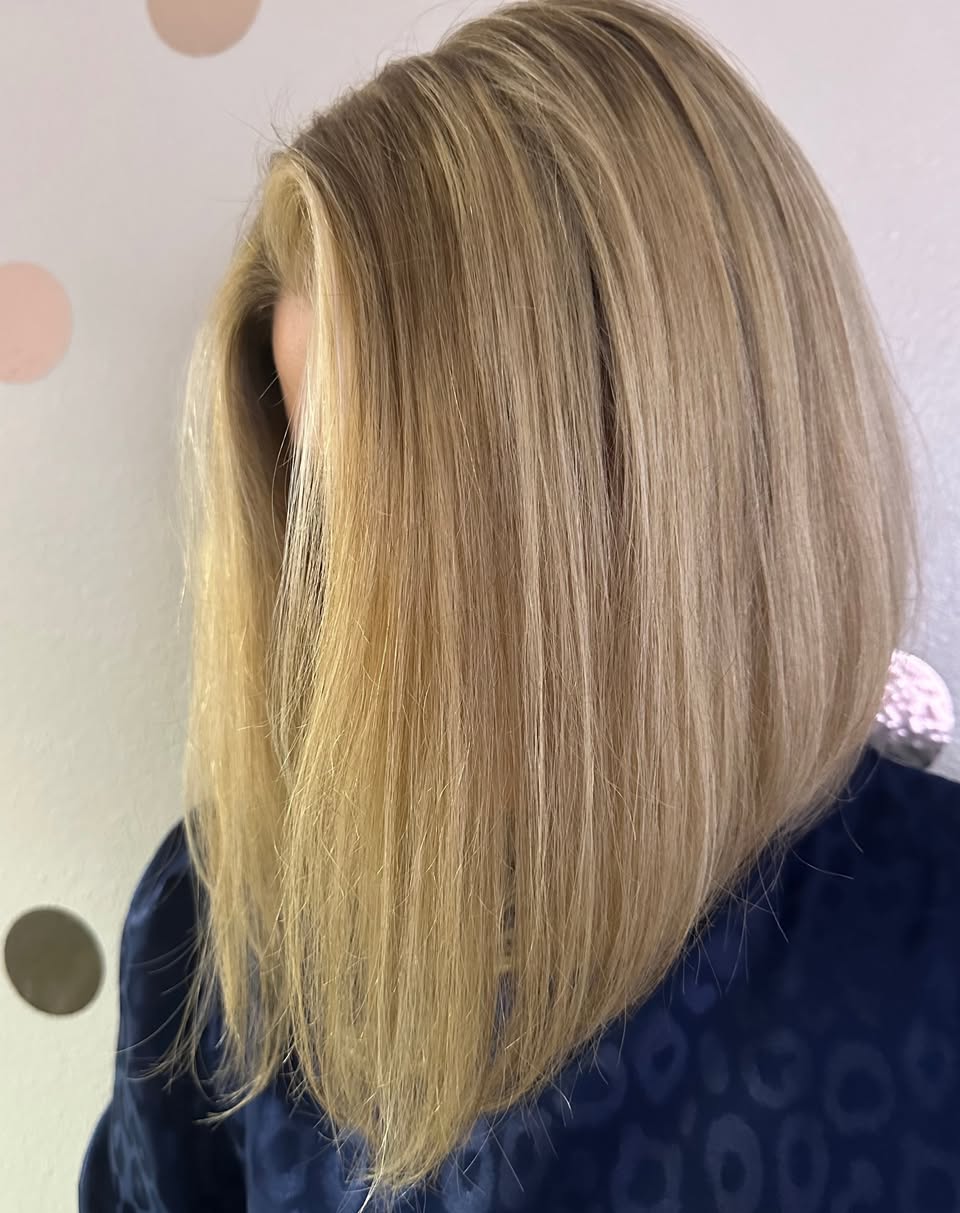 Side view of a person with straight, shoulder-length blonde hair, wearing a dark top.