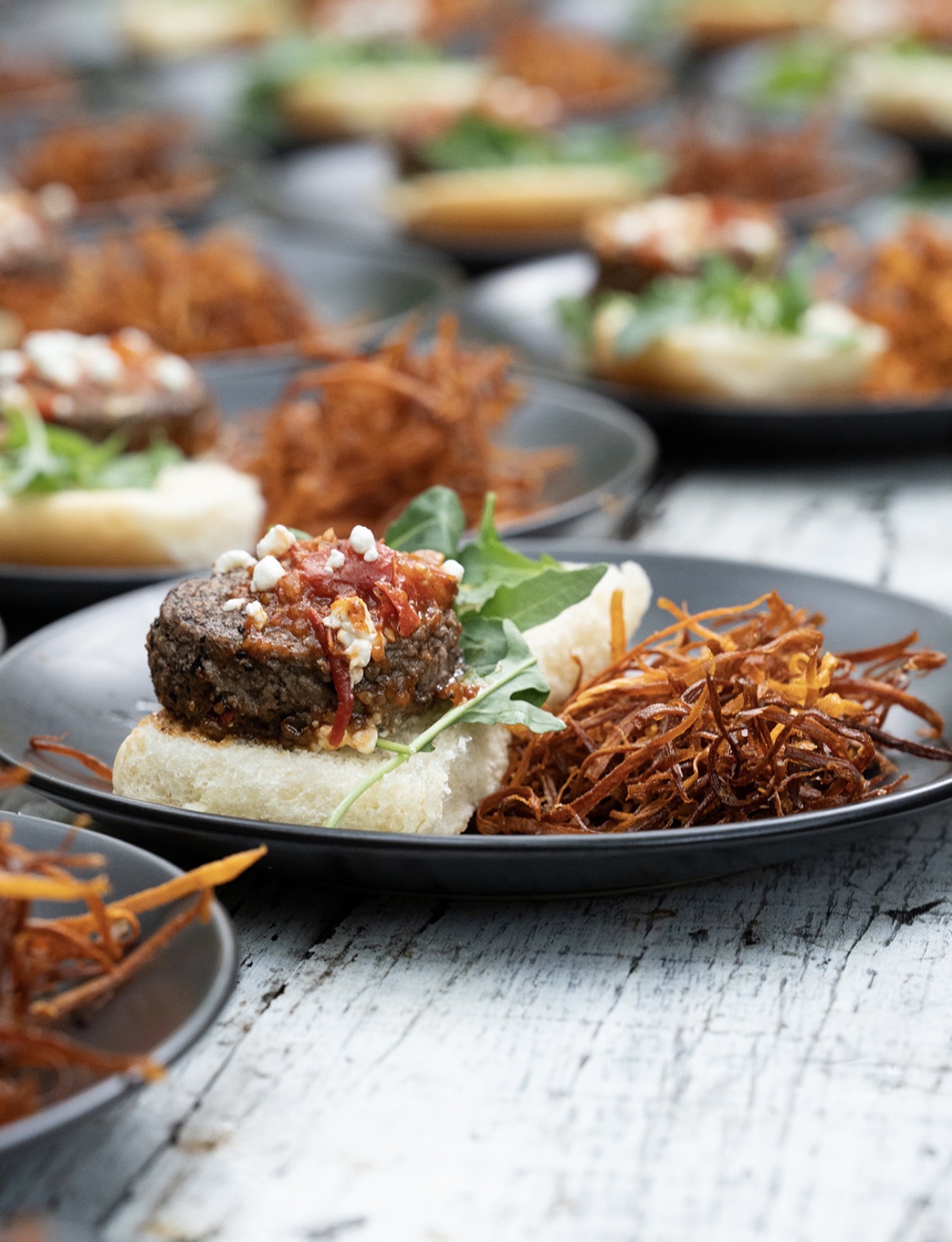 Plate with a meatball, lettuce, and shredded carrots on a white surface, with multiple similar plates in the background.