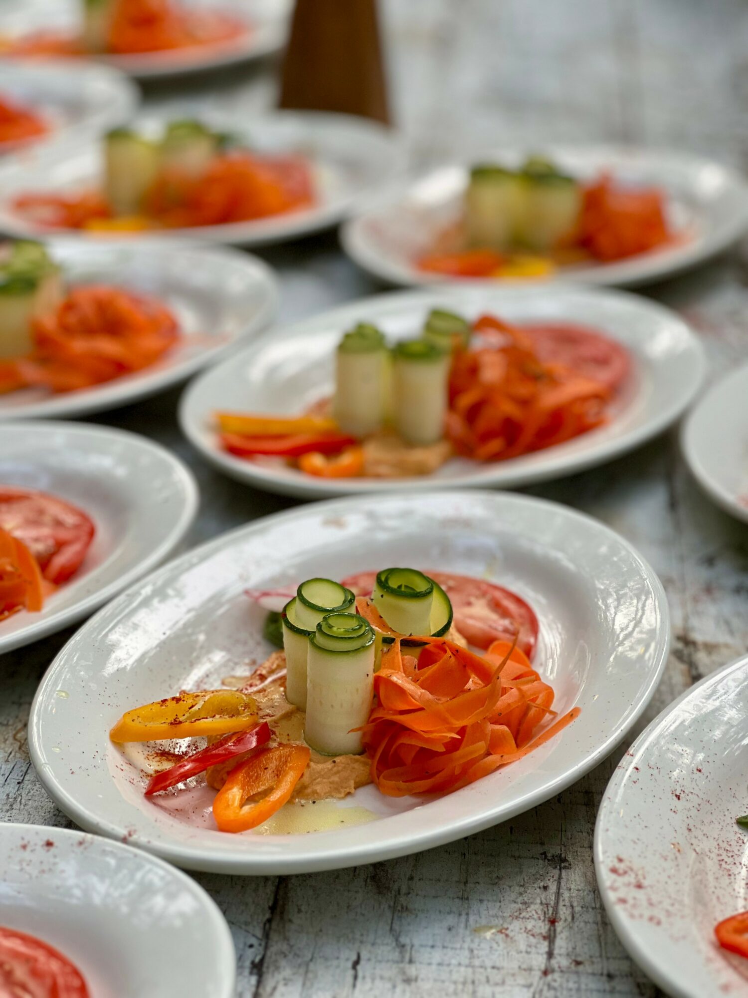 Multiple plates with sliced vegetables and rolled items on a rustic table, focus on one plate in foreground, colorful presentation.