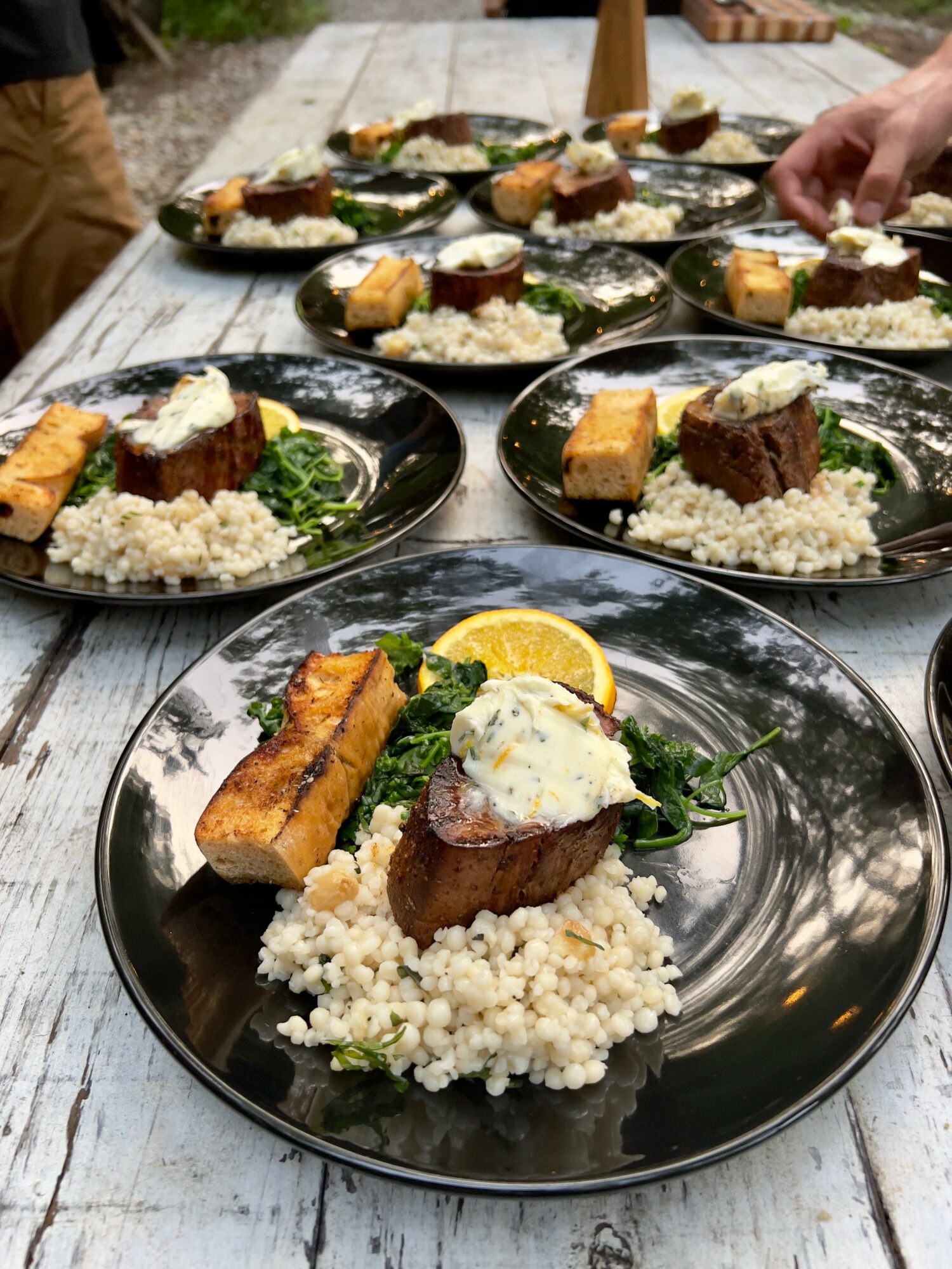 Plates with bread, rice, greens, lemon, and a dollop of sauce on a wooden table outdoors.