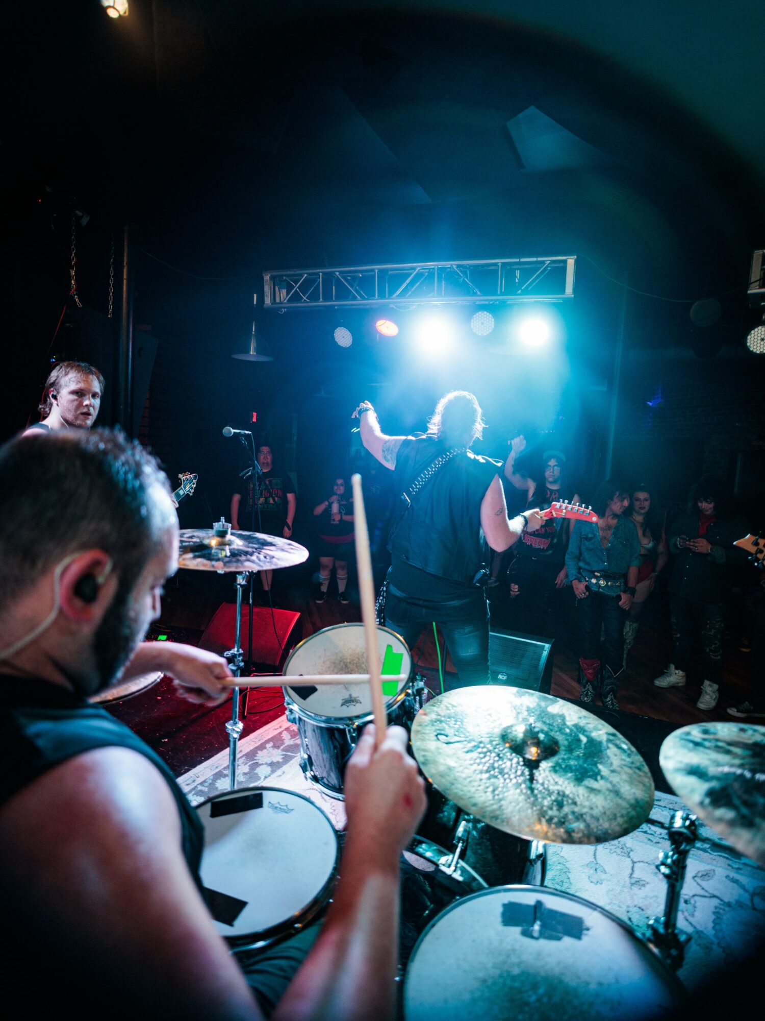 Musician playing drums at a concert with bright stage lights and audience in background.
