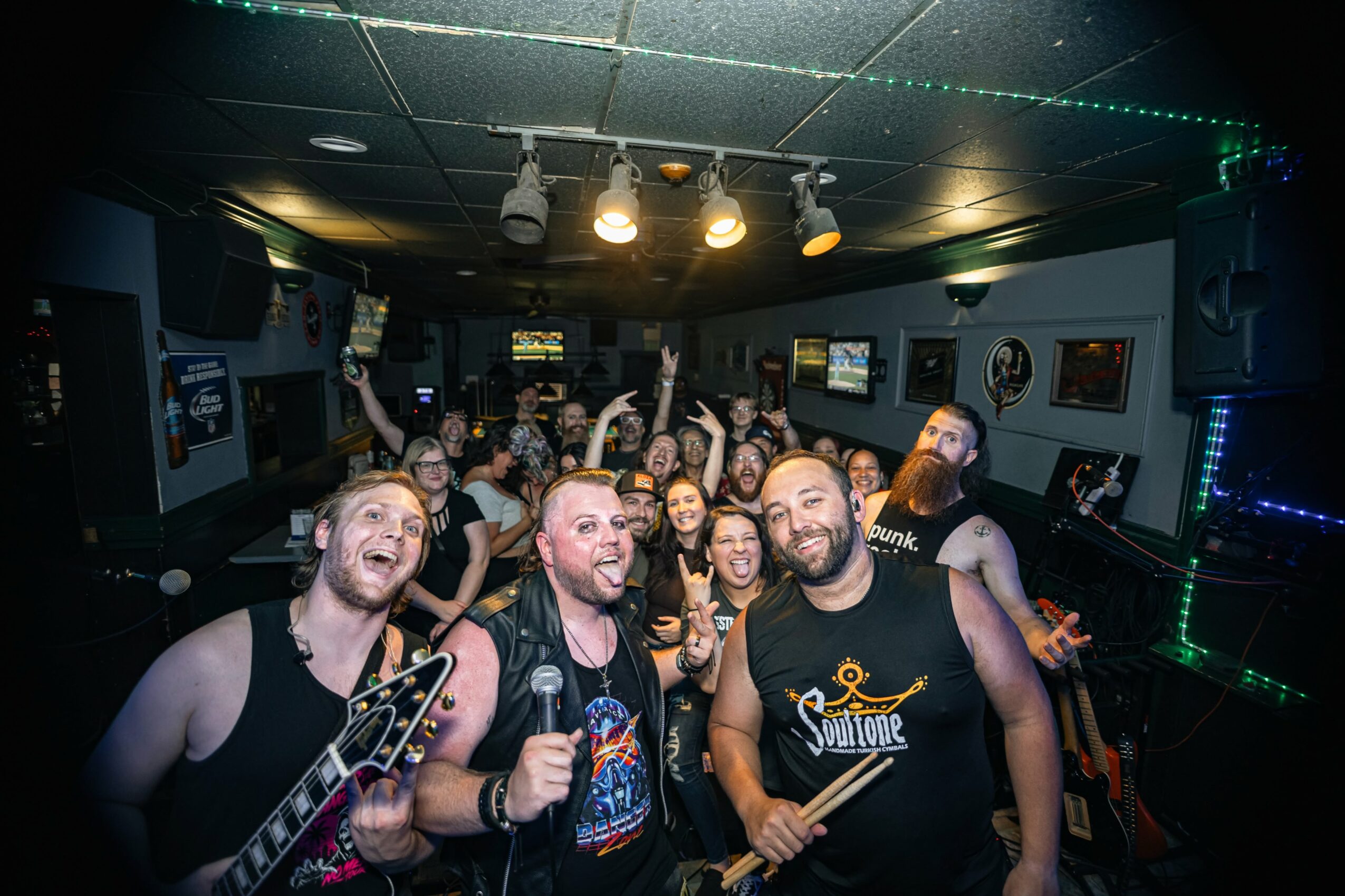 Group of people enjoying live music in a dimly lit venue, some holding instruments and raising hands.