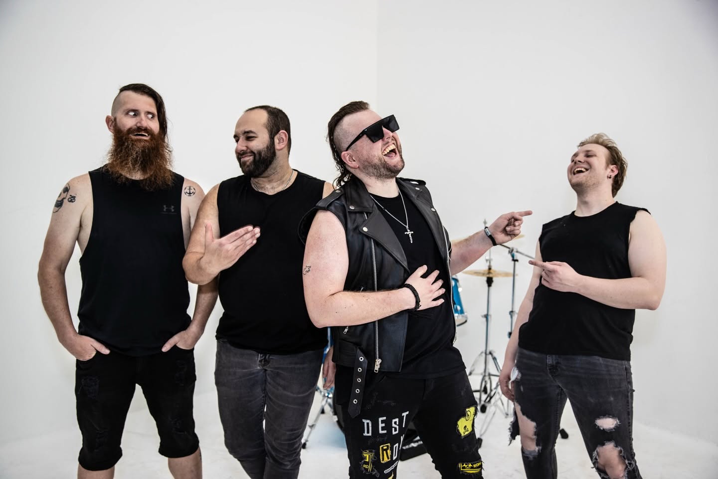 Four people laughing and talking, one wearing sunglasses and a leather vest, in a white studio space.