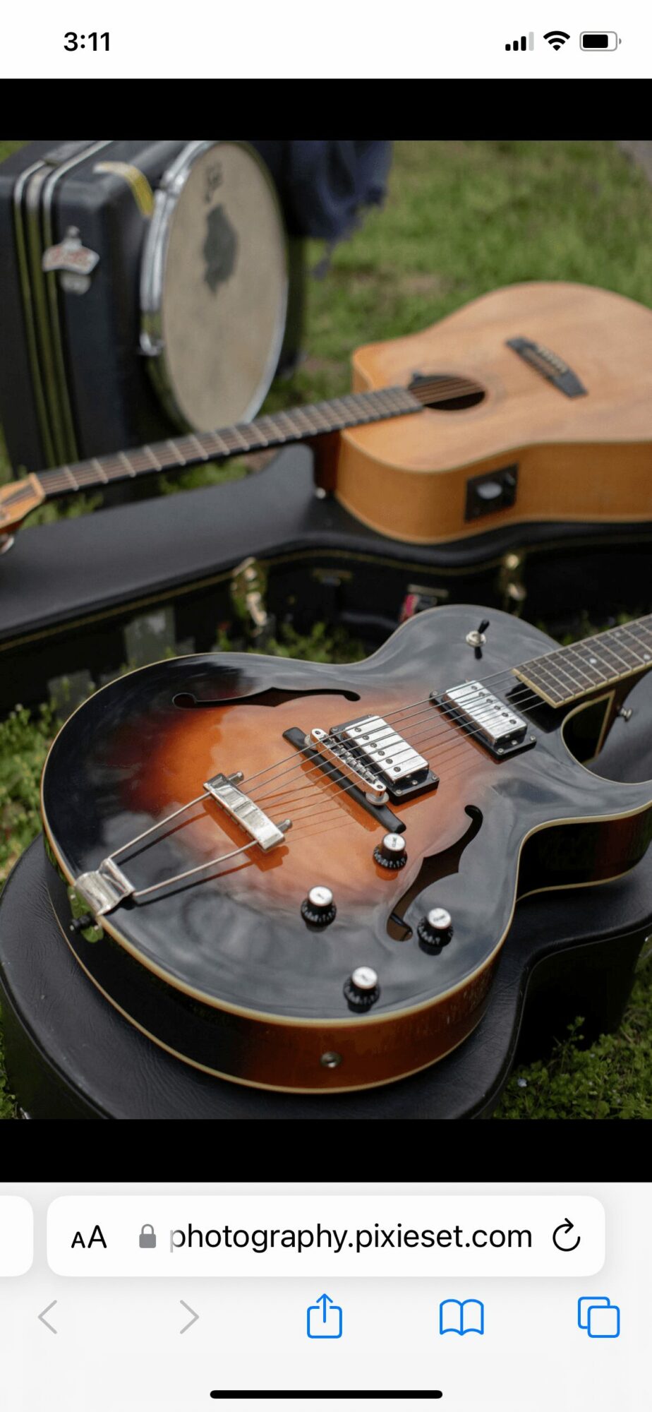 Two guitars in open cases outdoors on grass, one with a sunburst finish and the other with a natural wood finish.