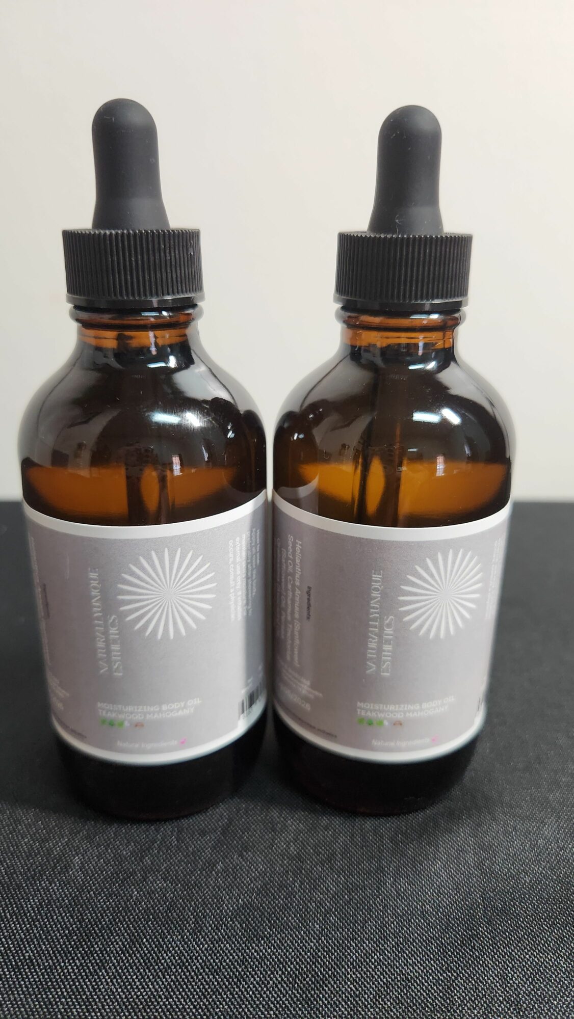 Two amber glass dropper bottles with black caps and white labels, lying on a dark surface.